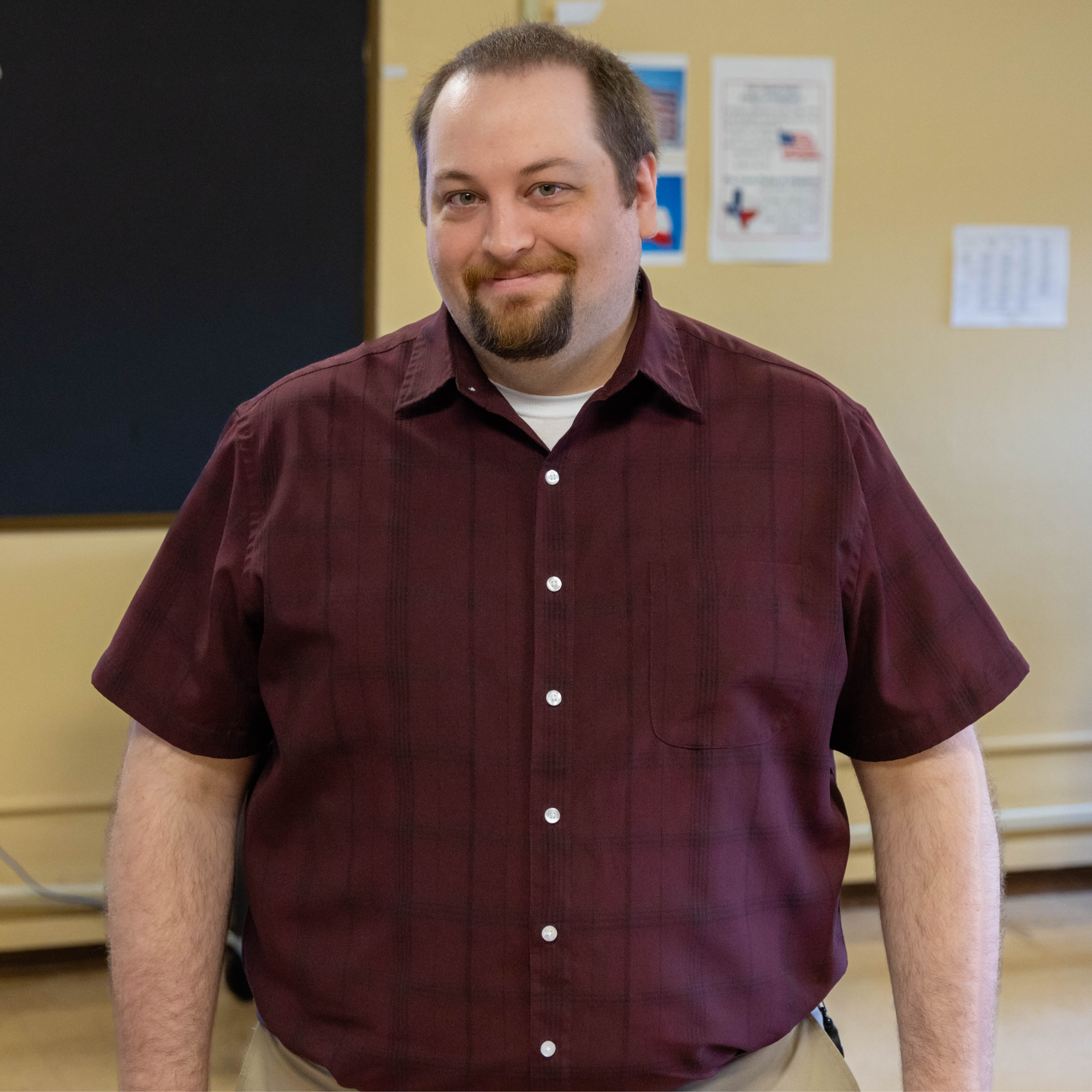 Caucasian man wearing a burgundy shirt standing in a classroom
