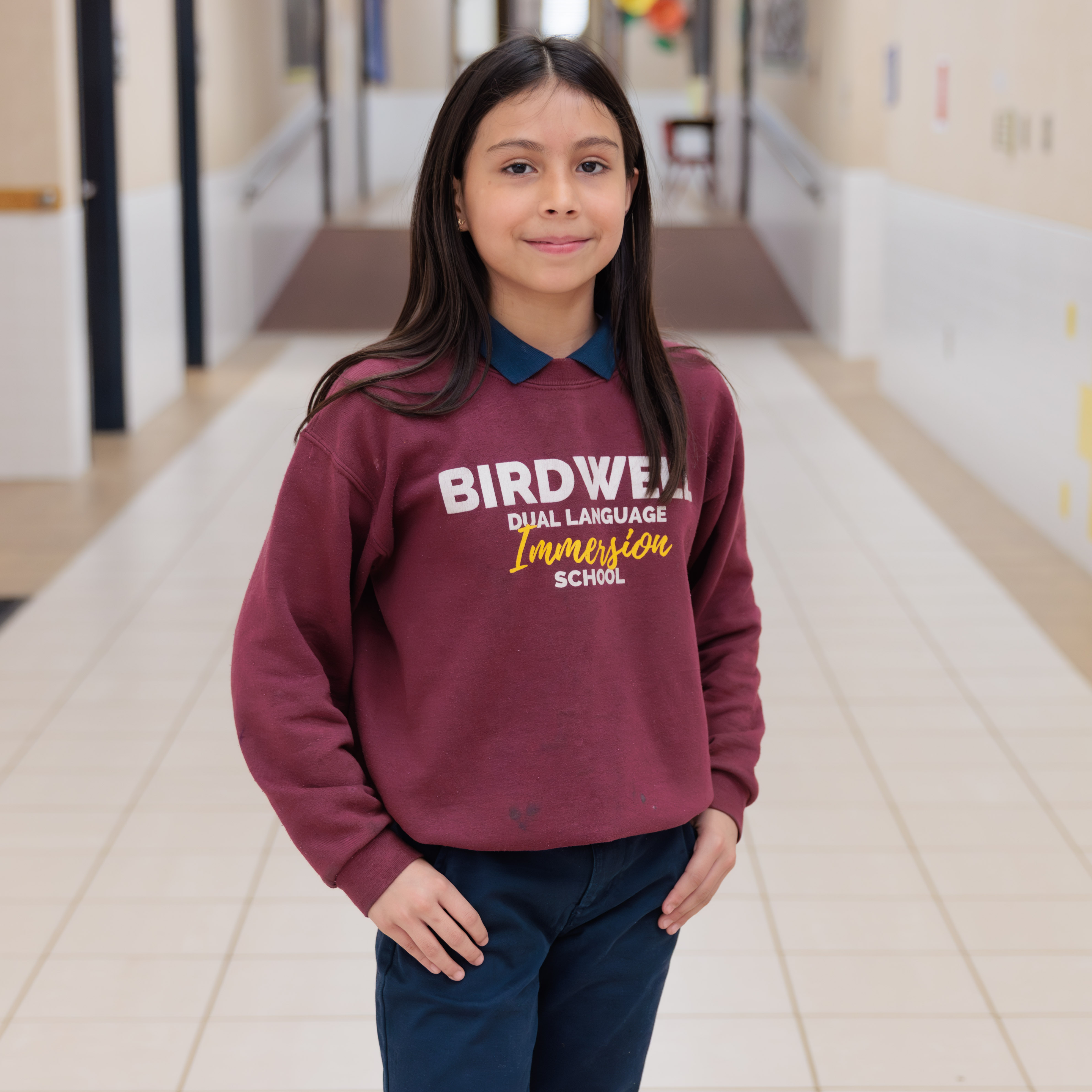 elementary age Hispanic girl wearing maroon sweatshirt and navy pants