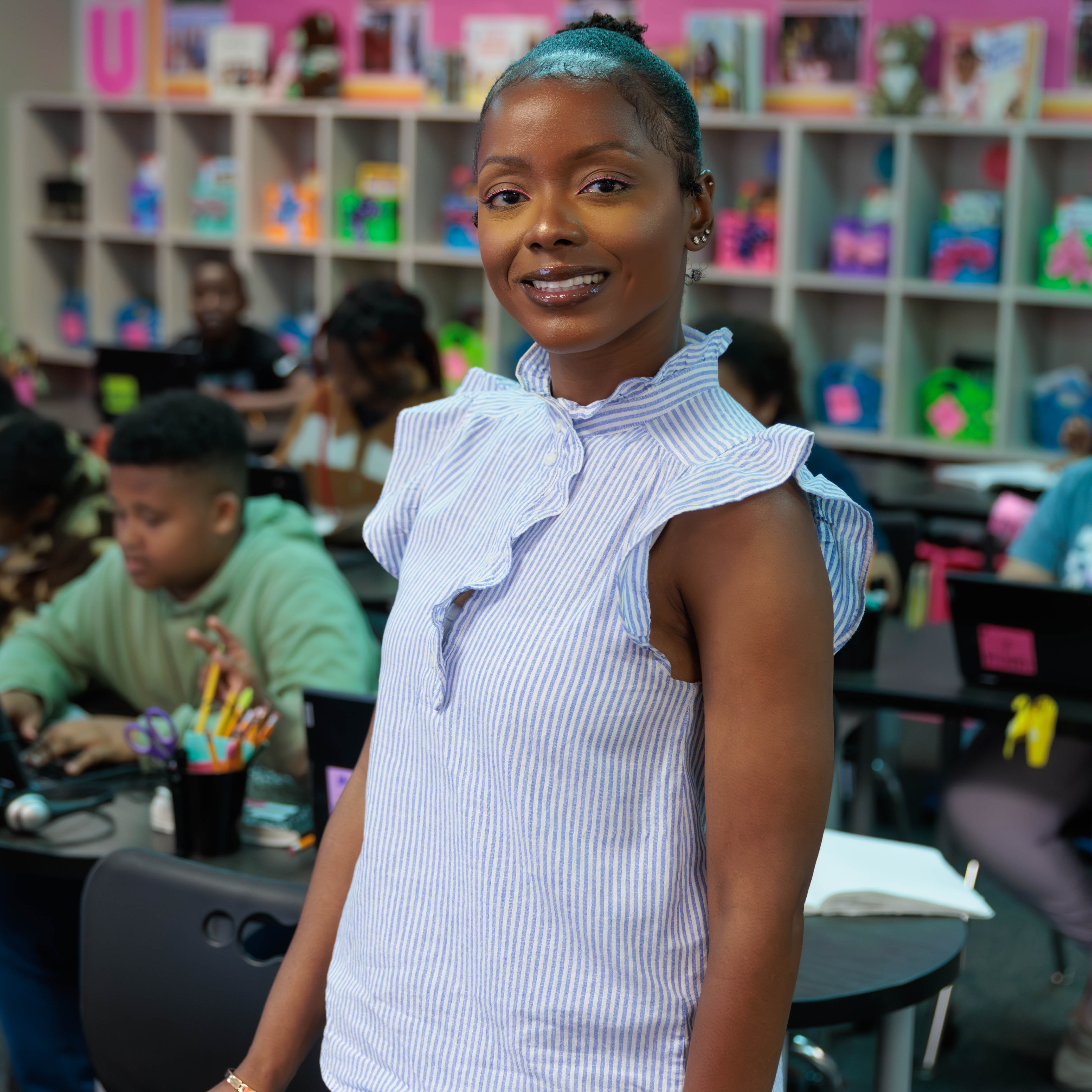 African American woman wearing a blue and white striped blouse standing in a classroom with students