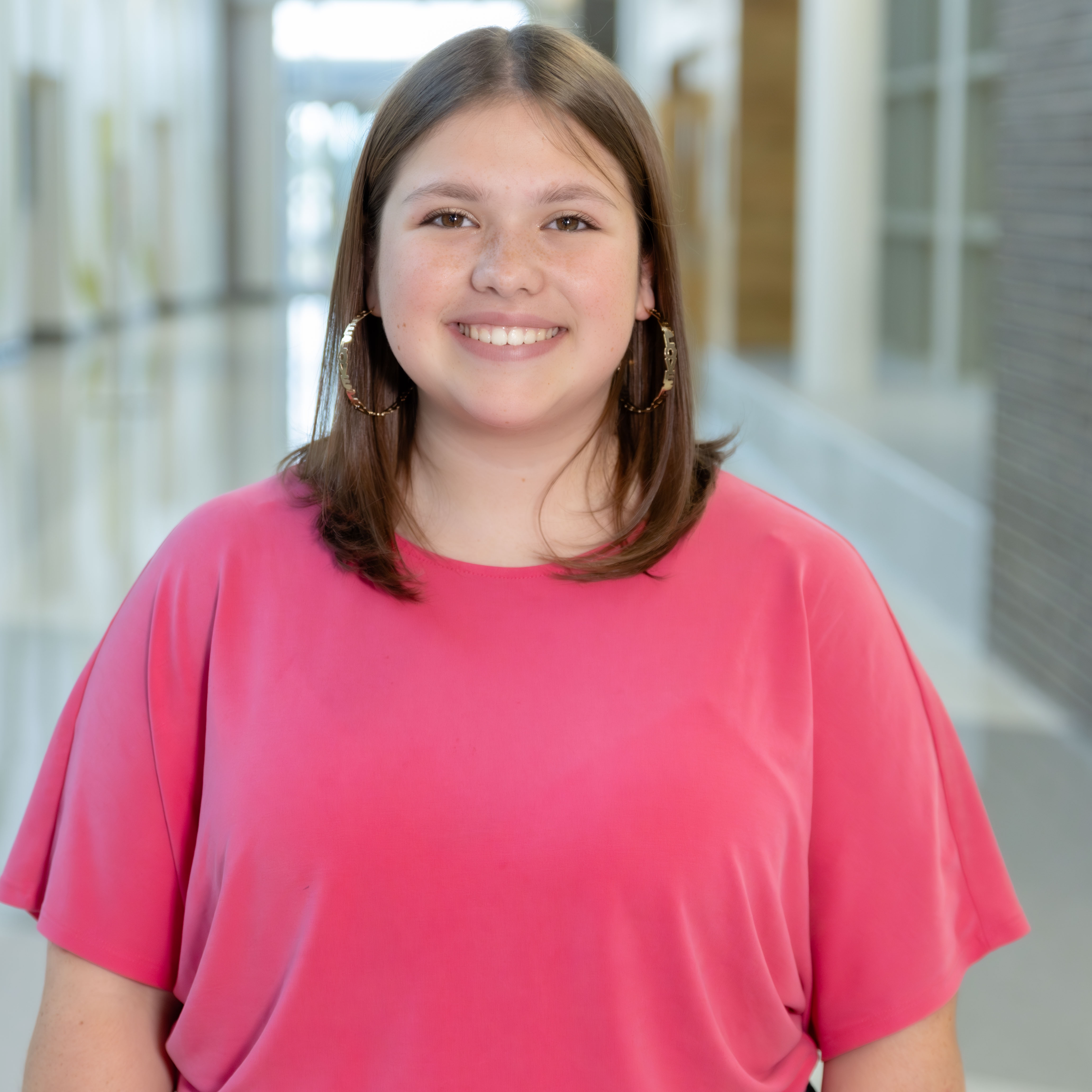 high school girl wearing a bright pink blouse standing in a school hallway