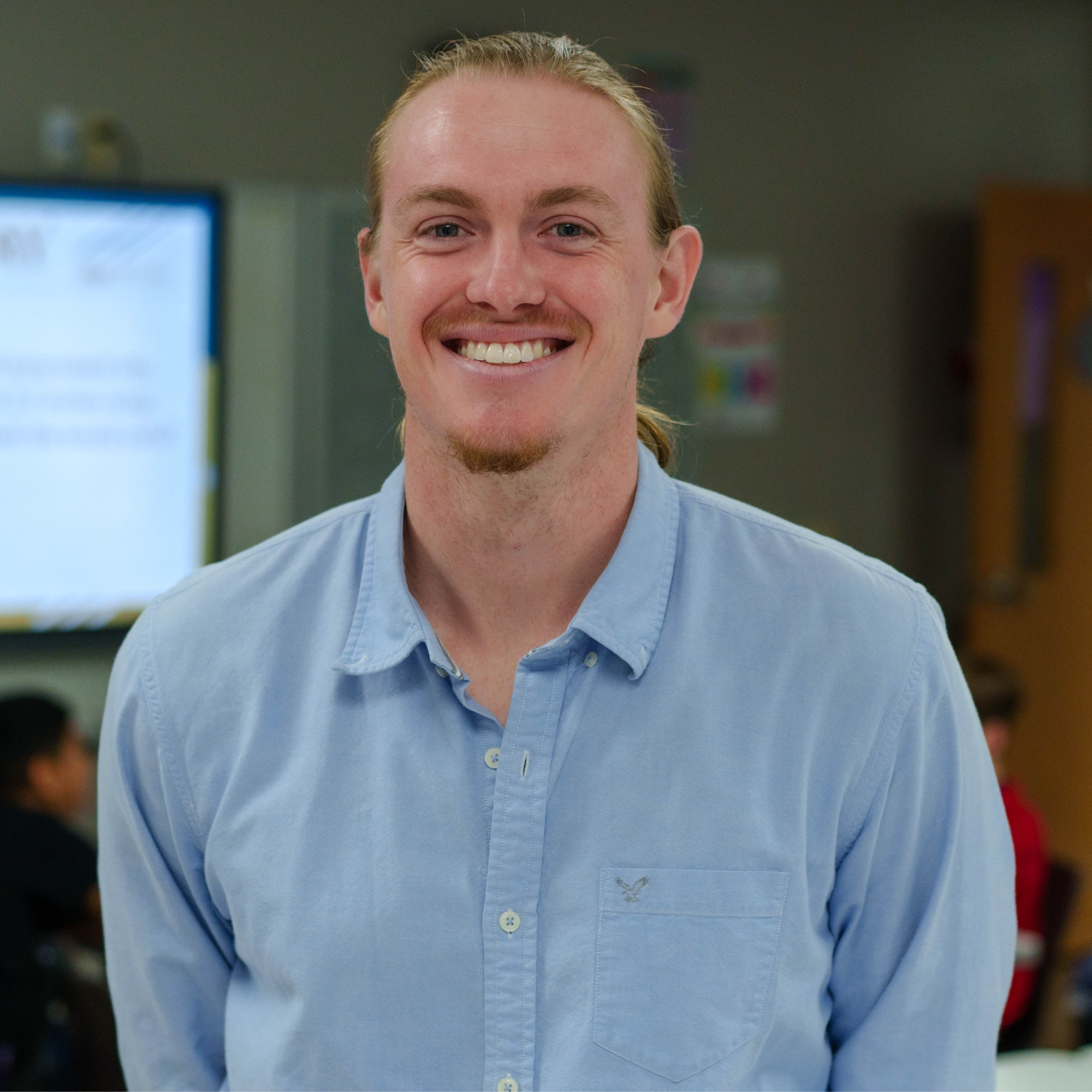 man wearing a blue button down shirt standing in a classroom