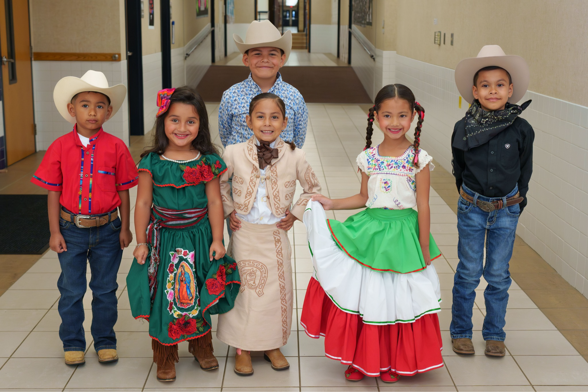 elementary age students and their Hispanic woman principal stand in a group wearing traditional Hispanic clothing