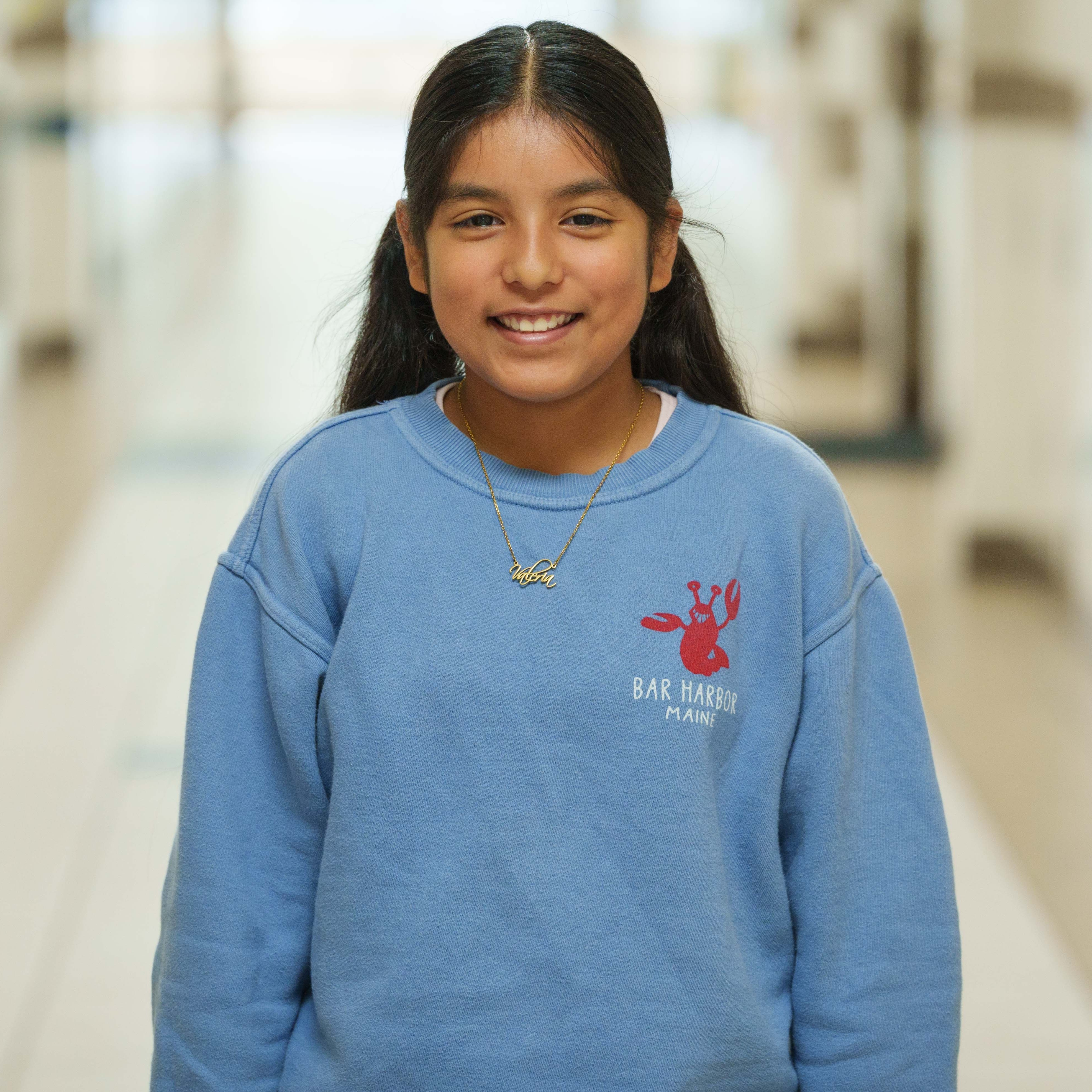 elementary age girl wearing blue sweatshirt standing in hallway