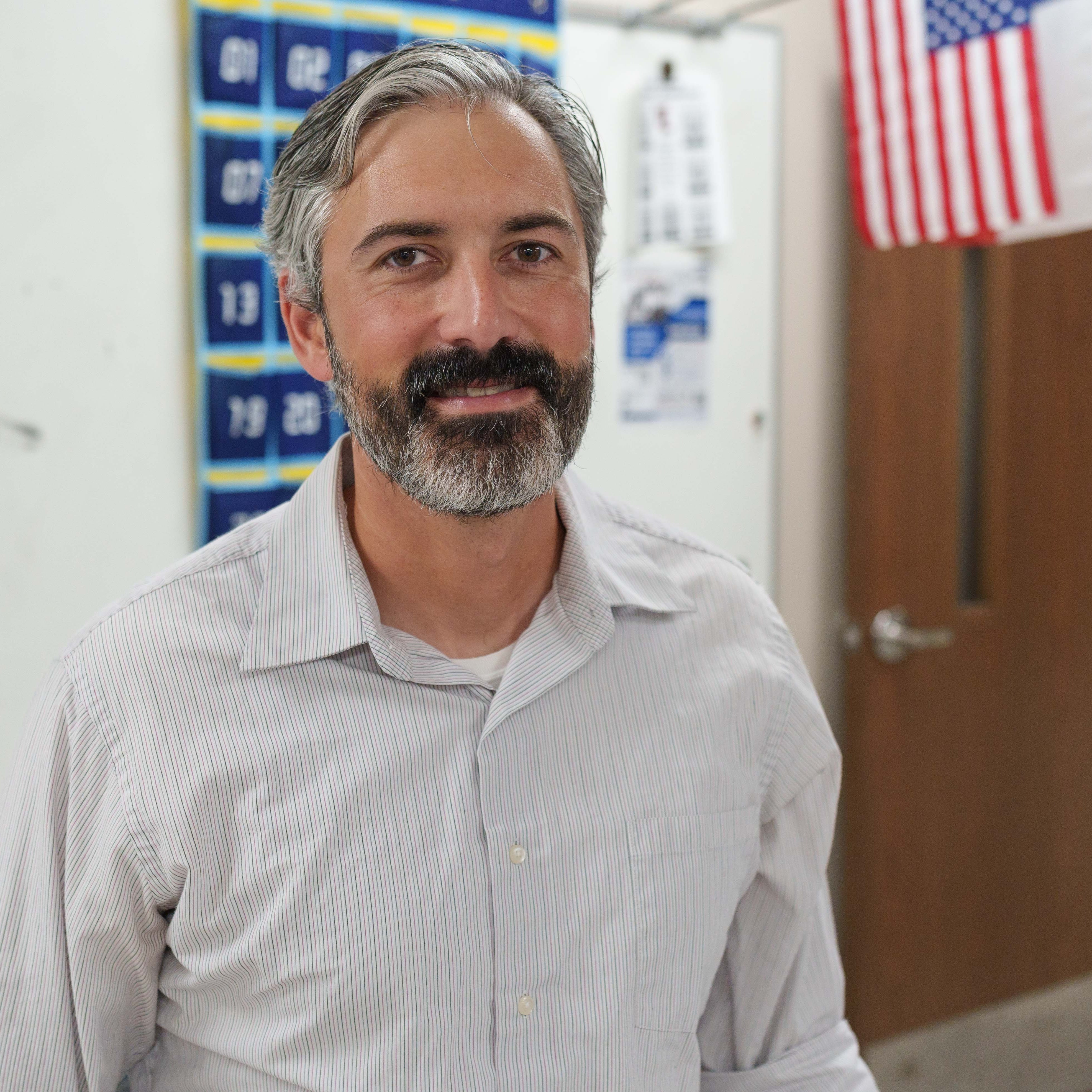 Caucasian man with gray hair and beard standing in classroom