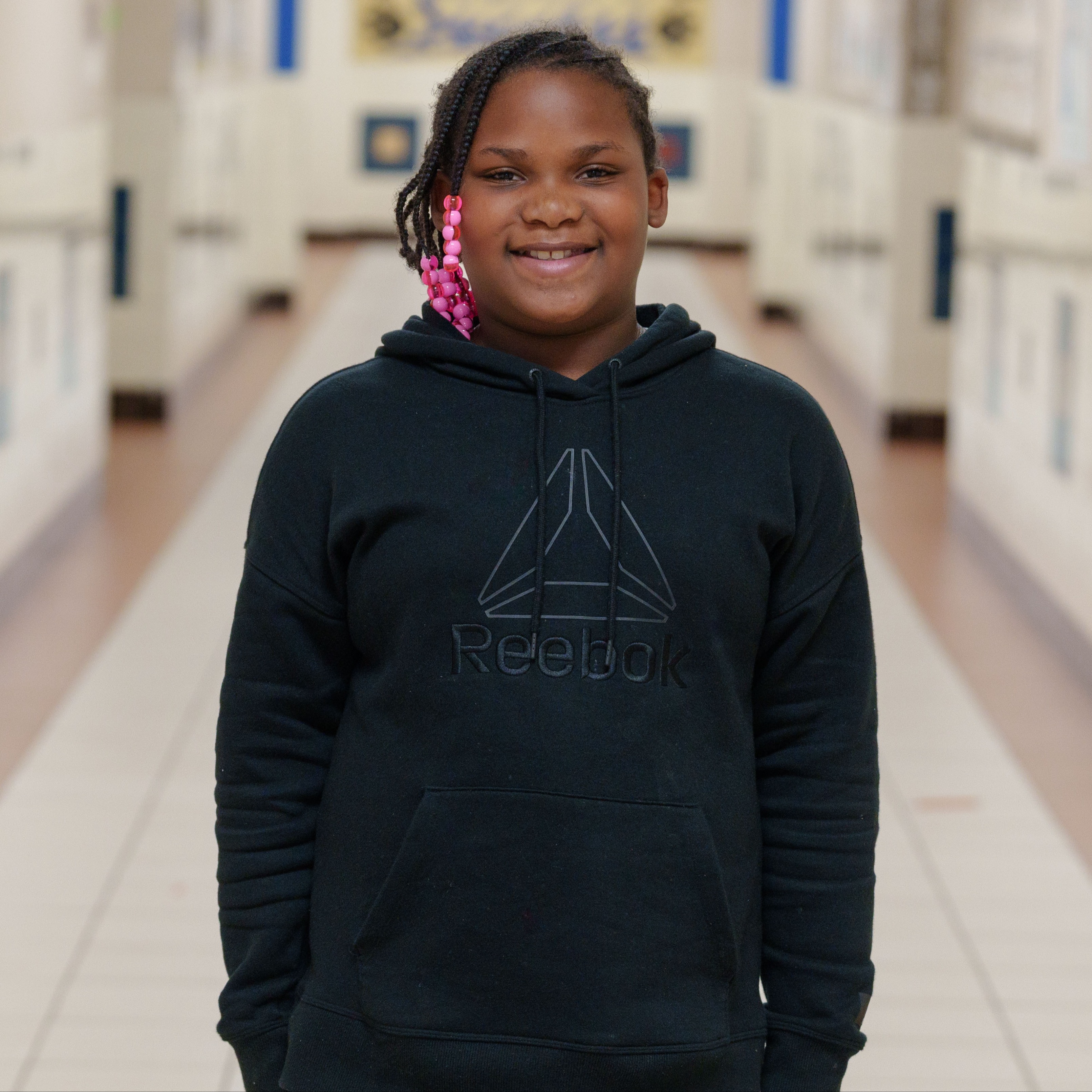 elementary age girl wearing a black hoodie standing in school hallway