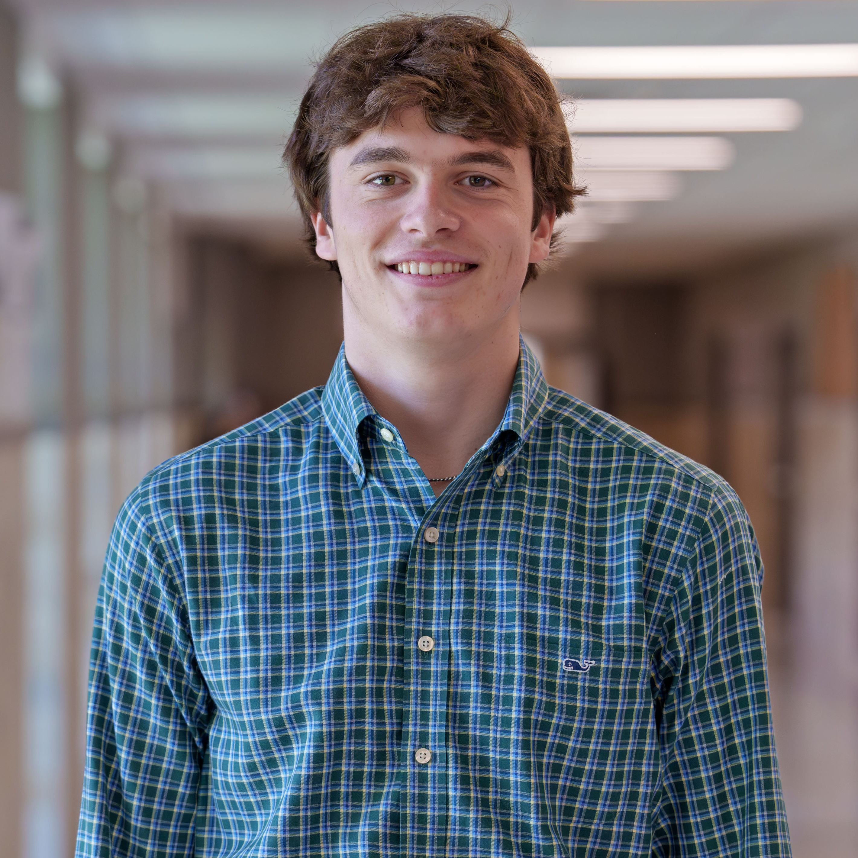 high school boy wearing plaid shirt standing in hallway