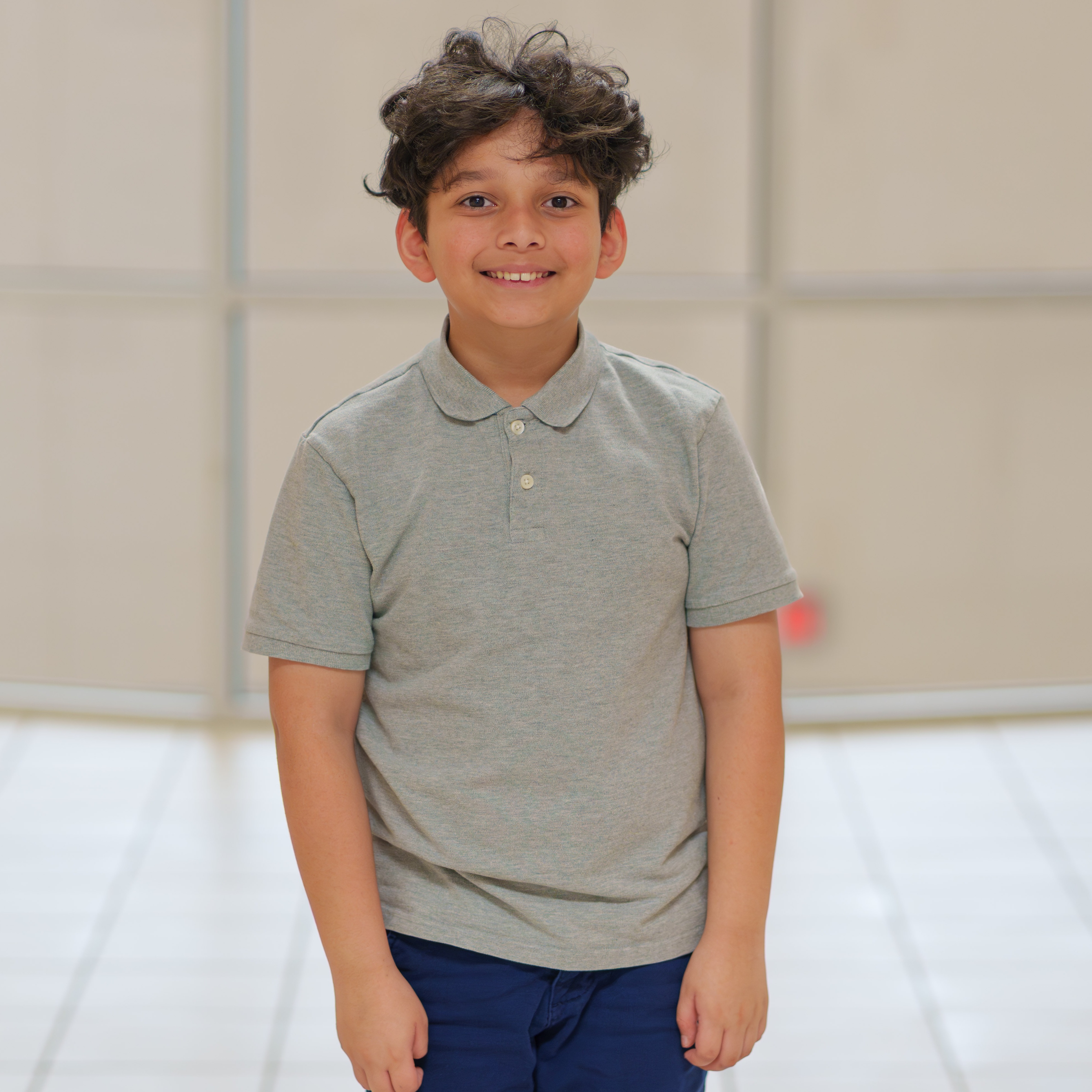 elementary age boy wearing tan shirt standing in hallway