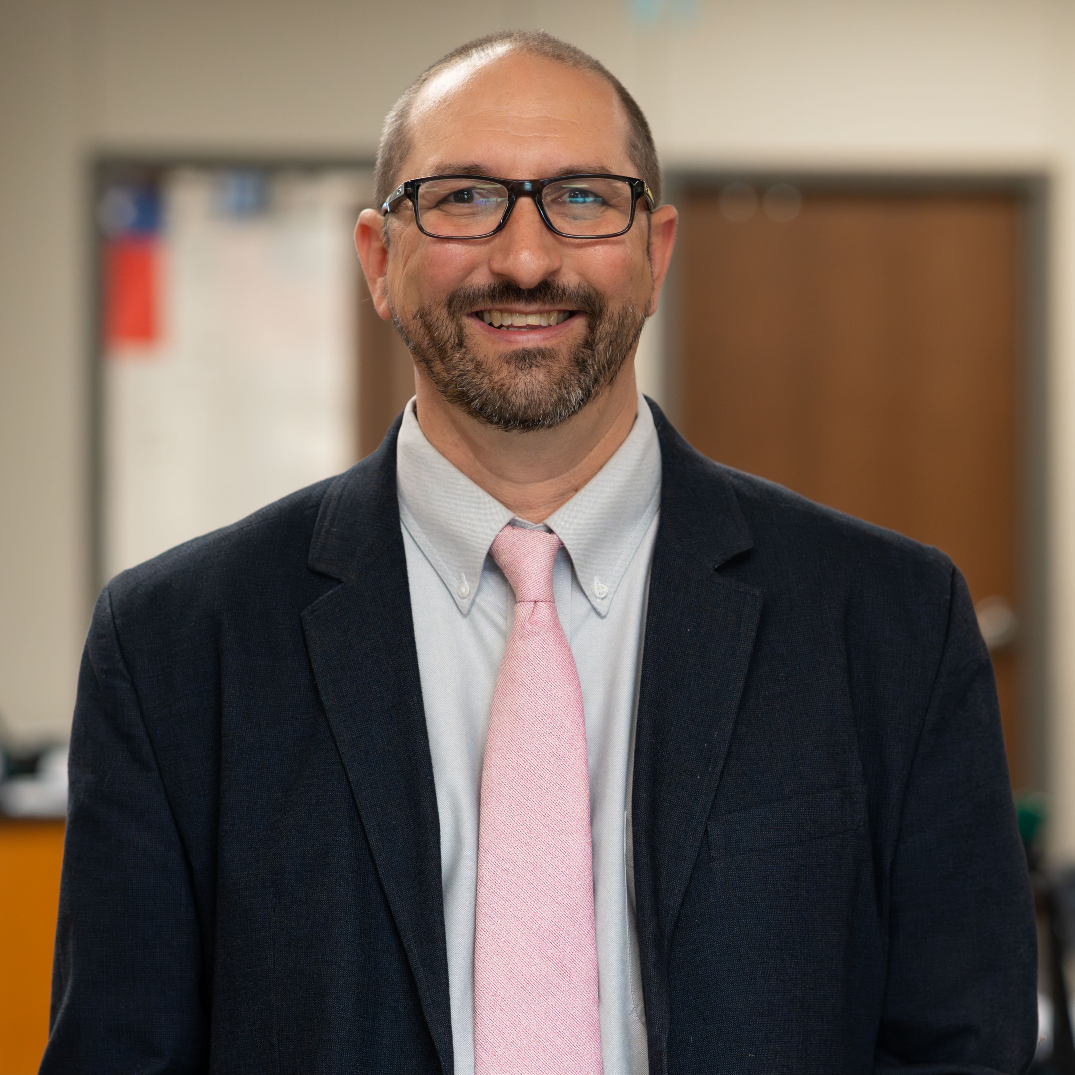 man with beard and glasses wearing a suit jacket with pink tie
