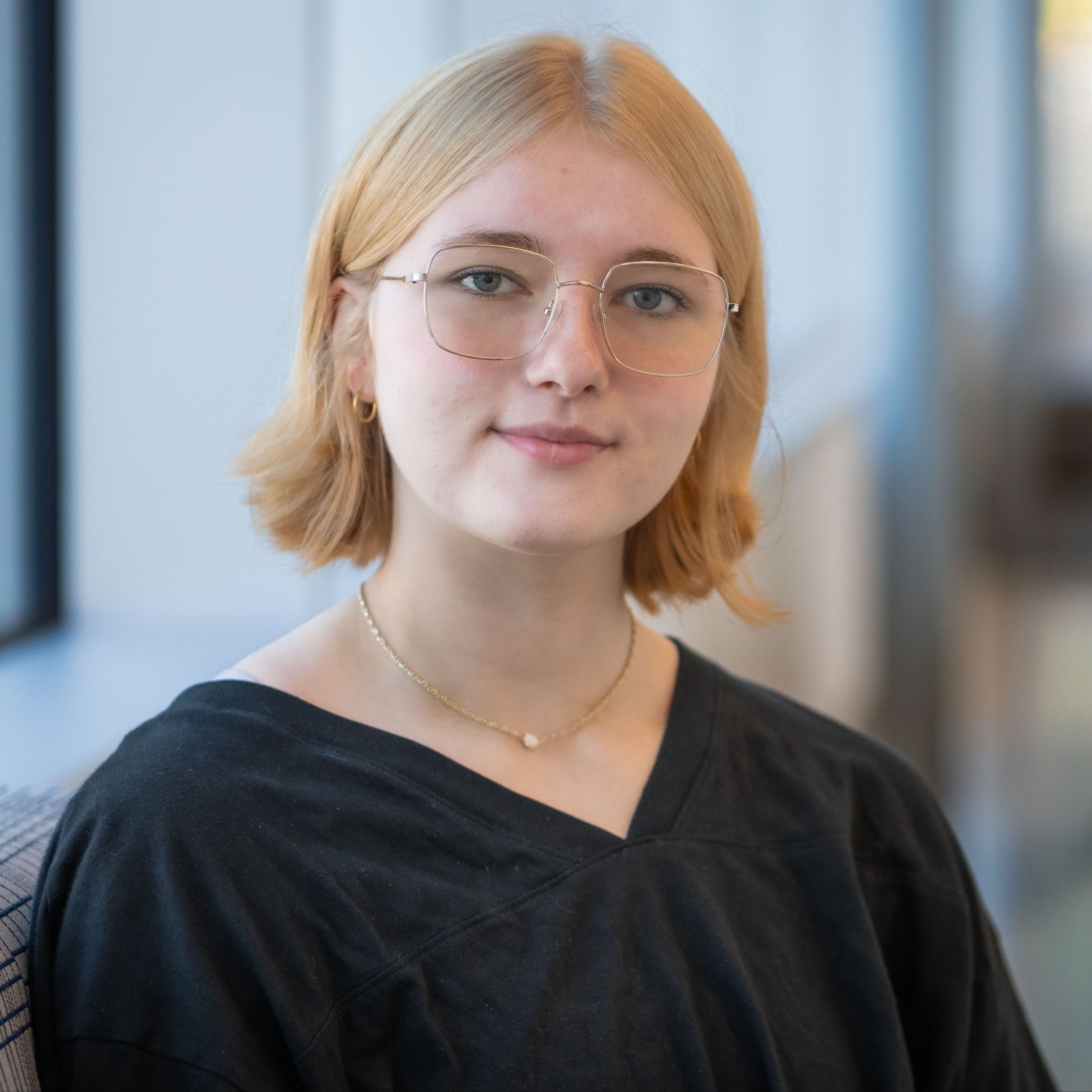 high school girl with short blonde hair and glasses wearing a black blouse
