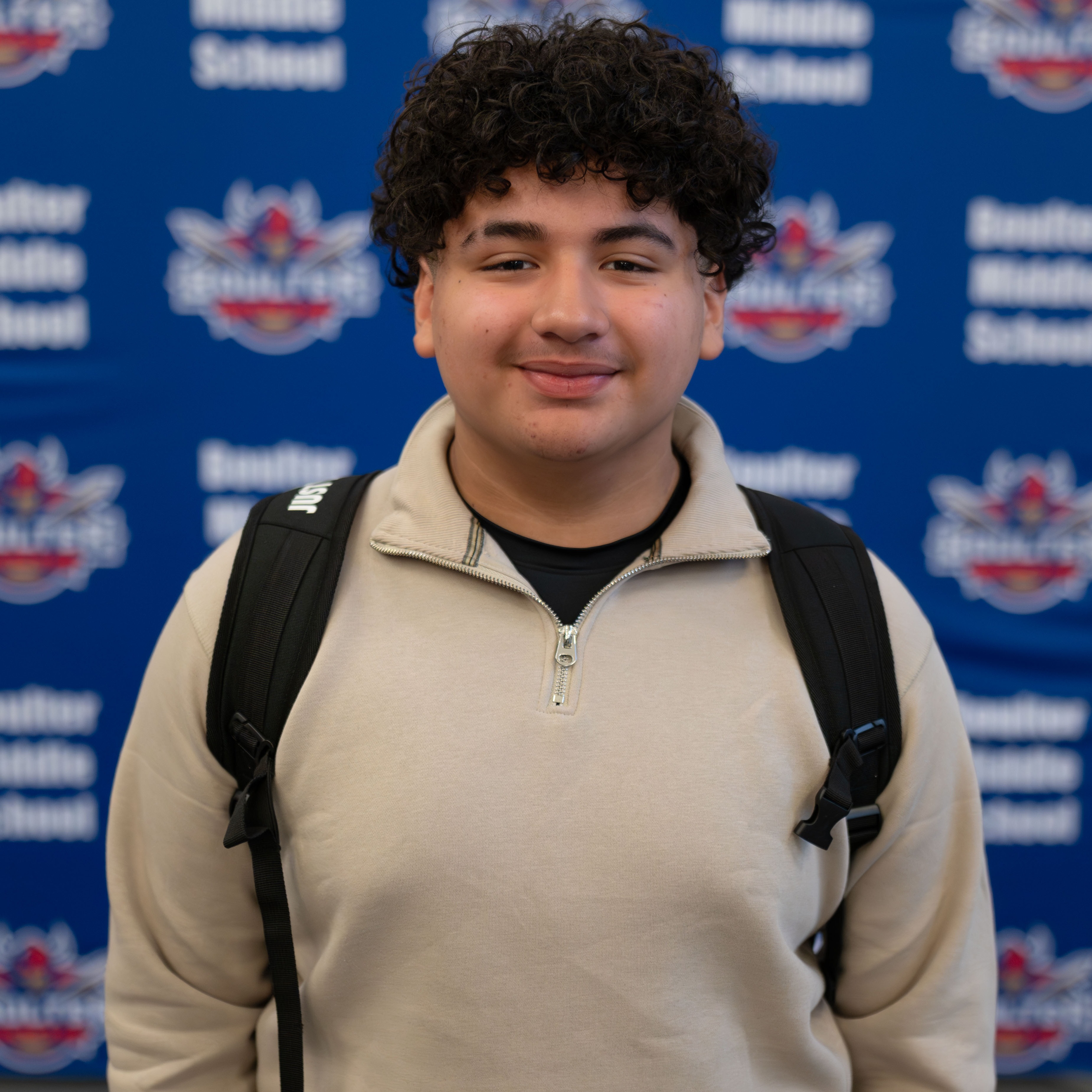 teen boy with dark curly hair and a backpack on smiling at camera