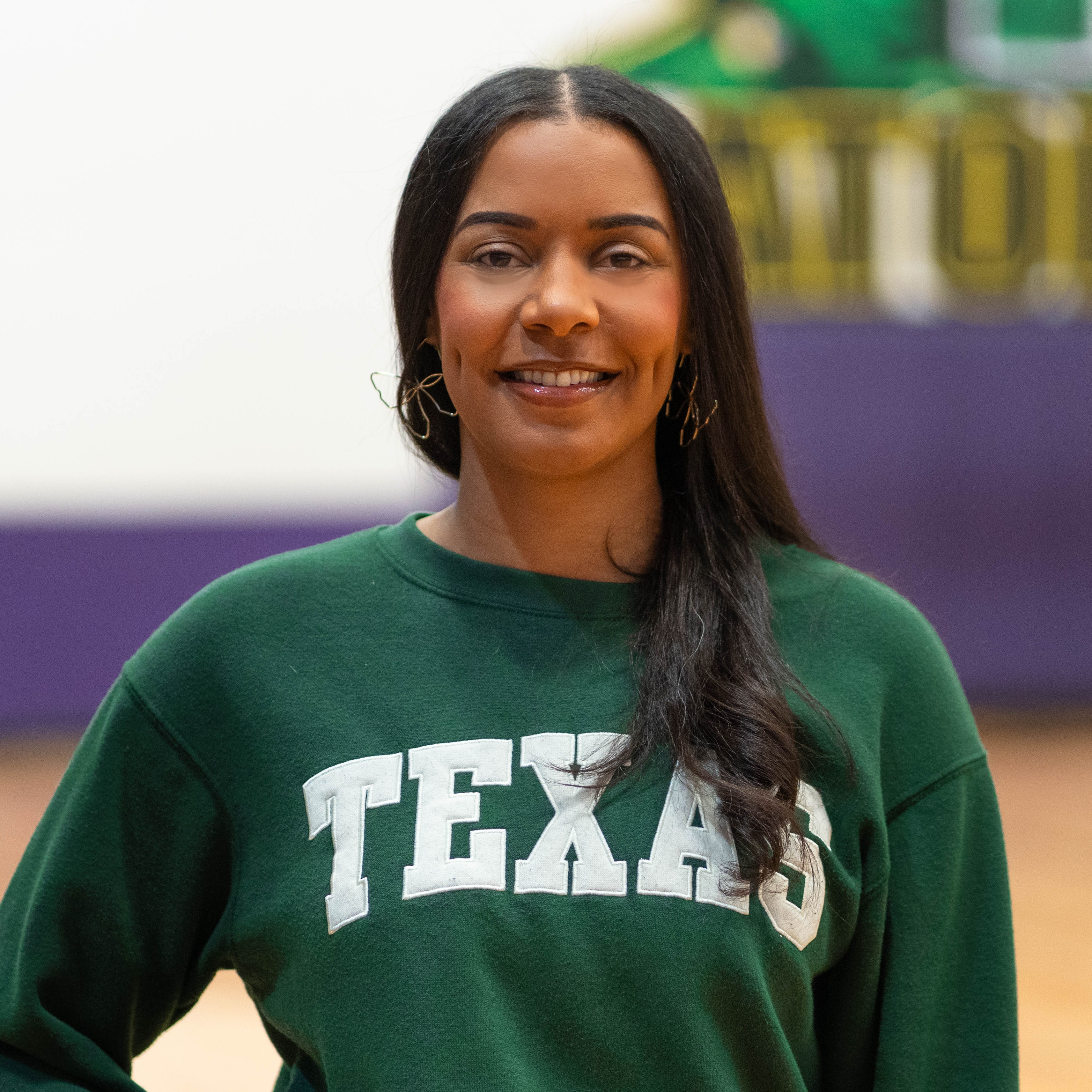 woman with long dark hair wearing green TEXAS sweatshirt smiling