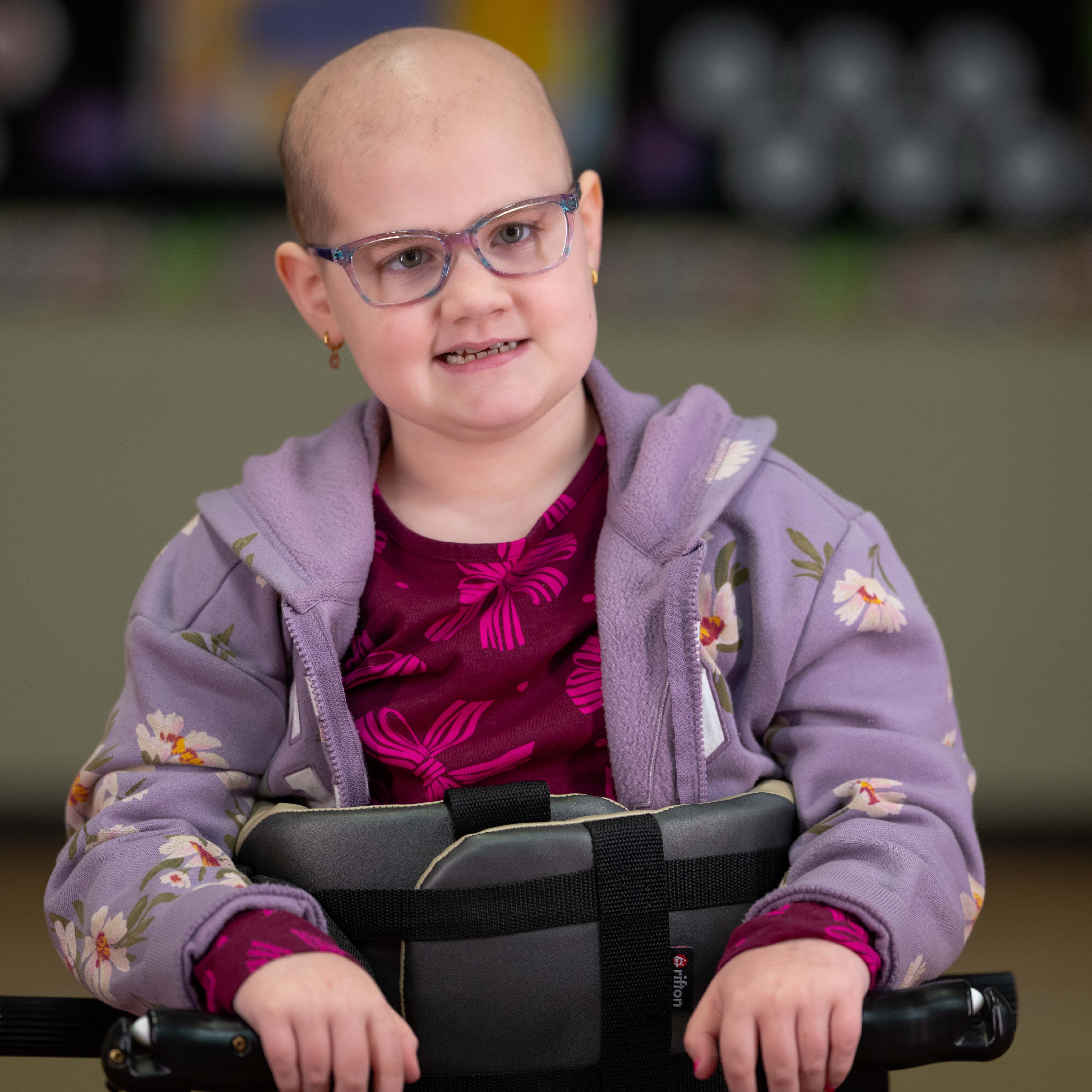elementary age girl with bald head and glasses smiling
