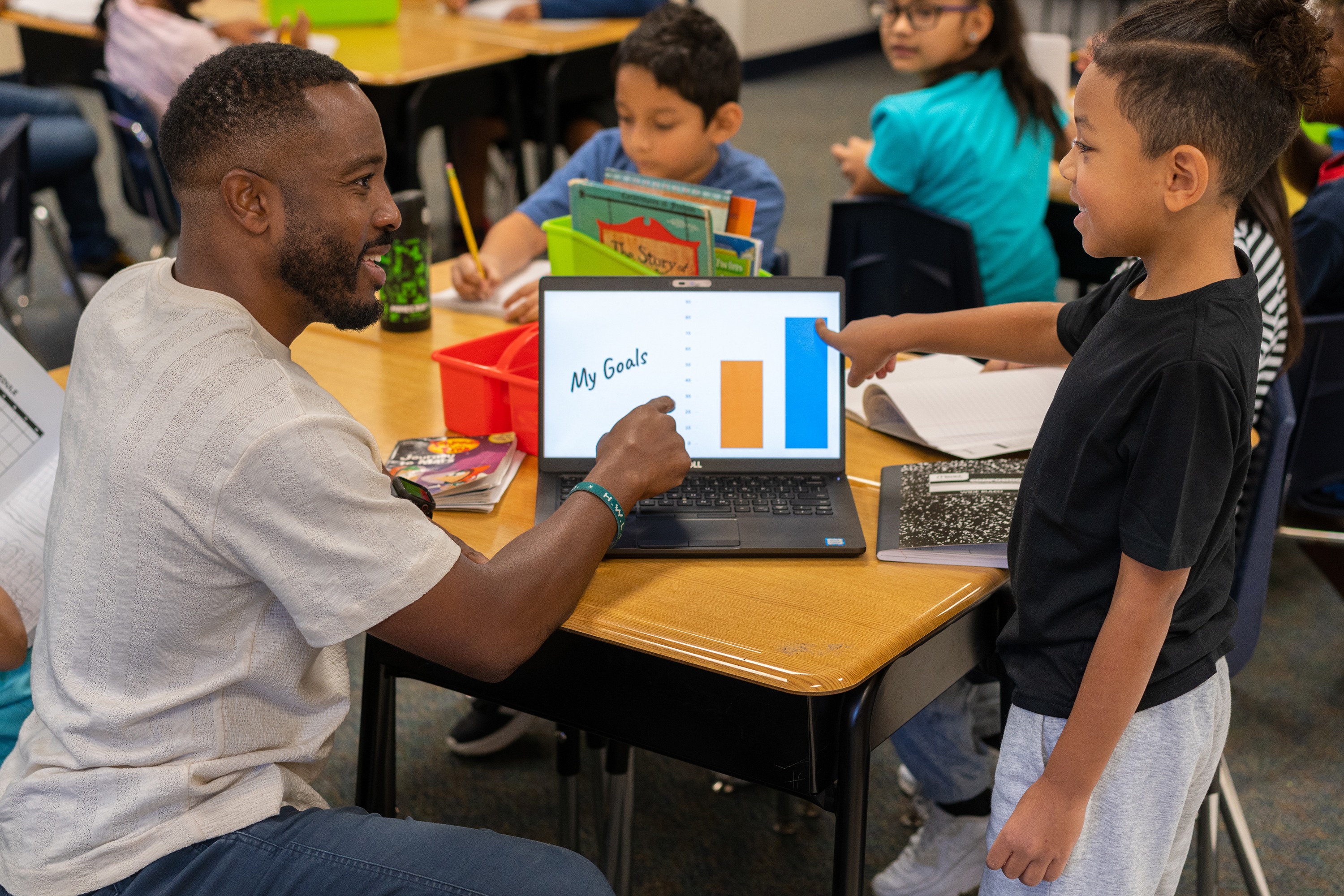 man and elementary age kids looking at laptop in classroom