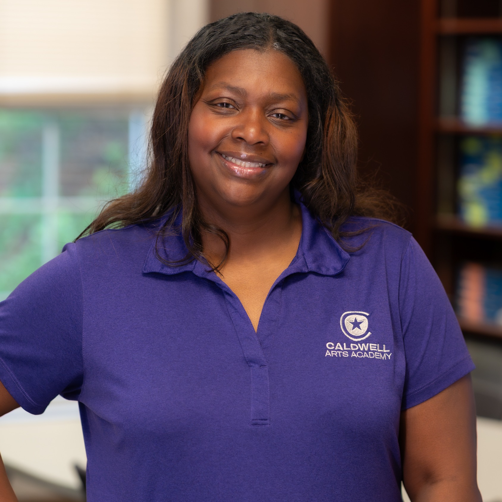 African American woman wearing a purple polo standing in her classroom 