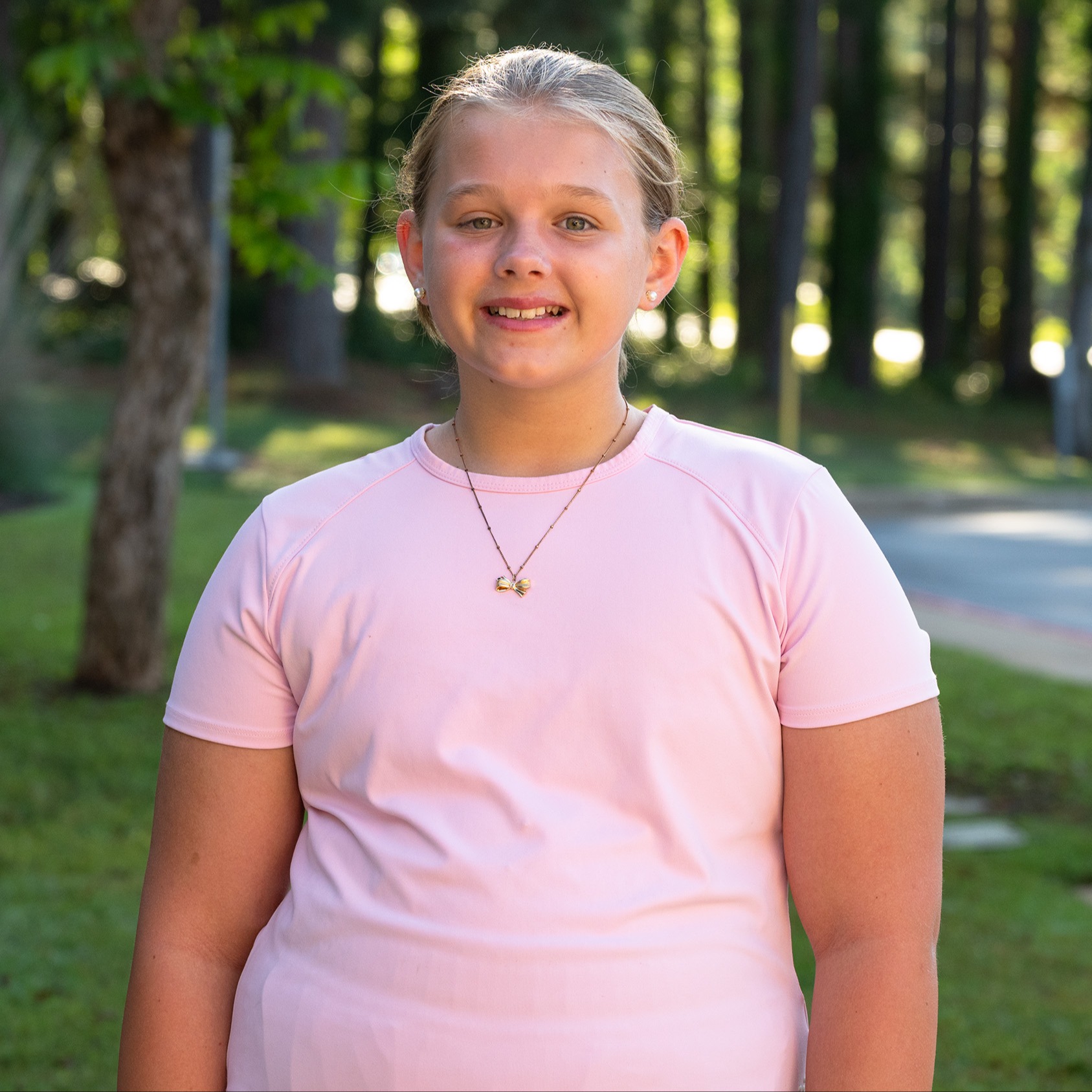 elementary age girl wearing pink tee standing in grassy yard 