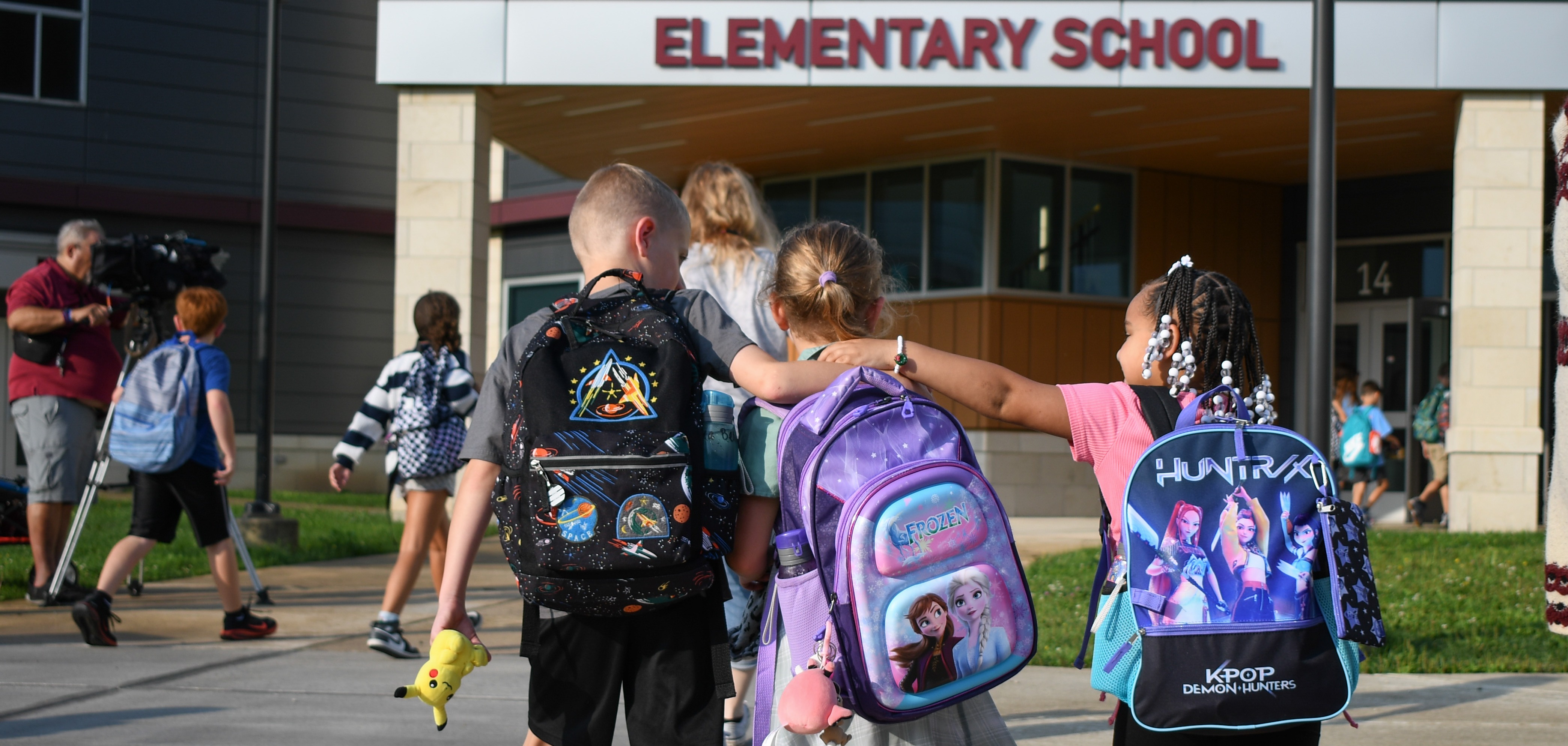 Students walk into elementary school with arms around each other