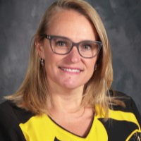 headshot of Mrs. Shimkus with blond, shoulder-length hair and glasses, smiling in a black and yellow batman shirt