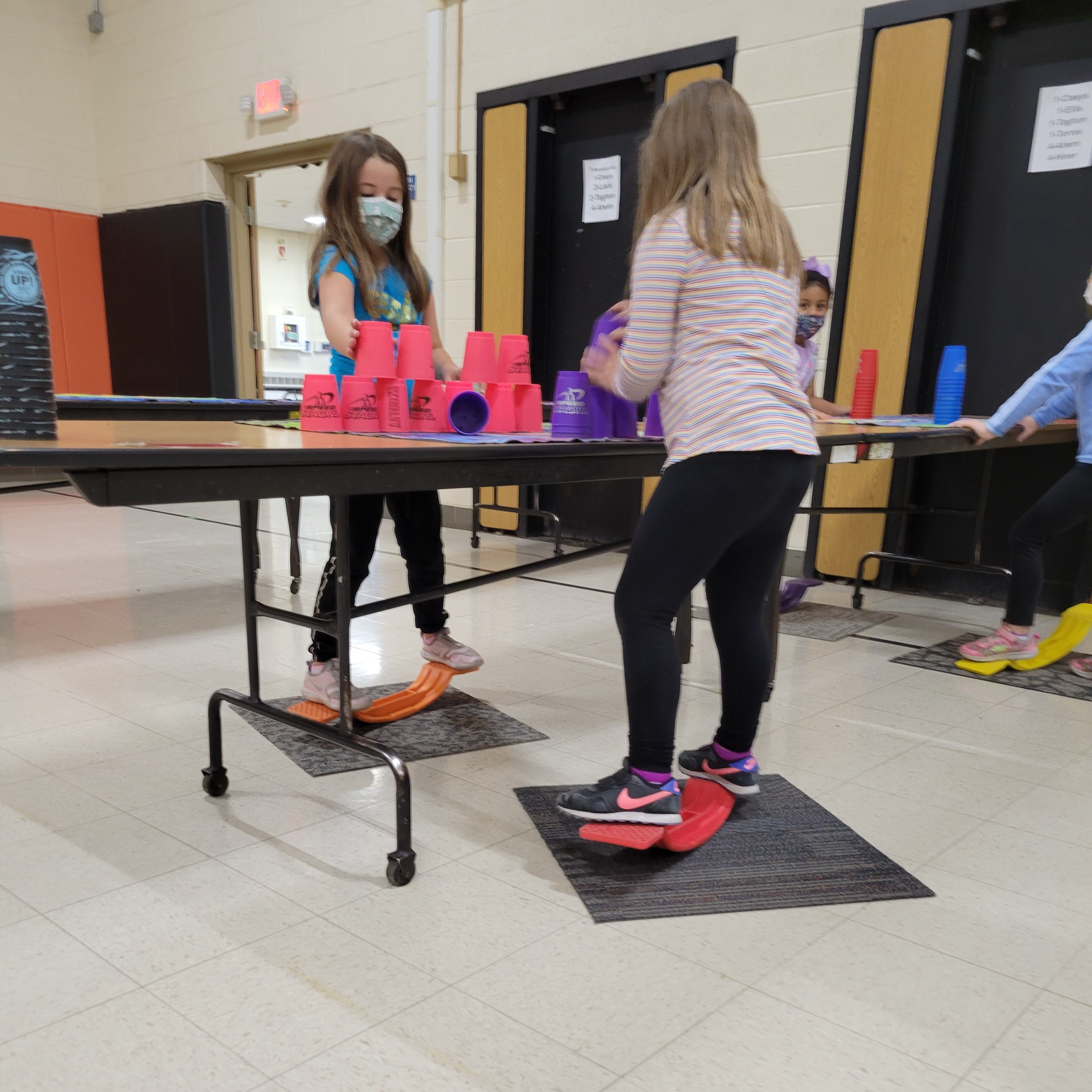 girls stacking cups separately while standing on a balance board