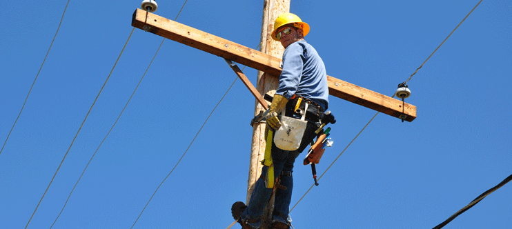 Man with hard hat up a power line pole
