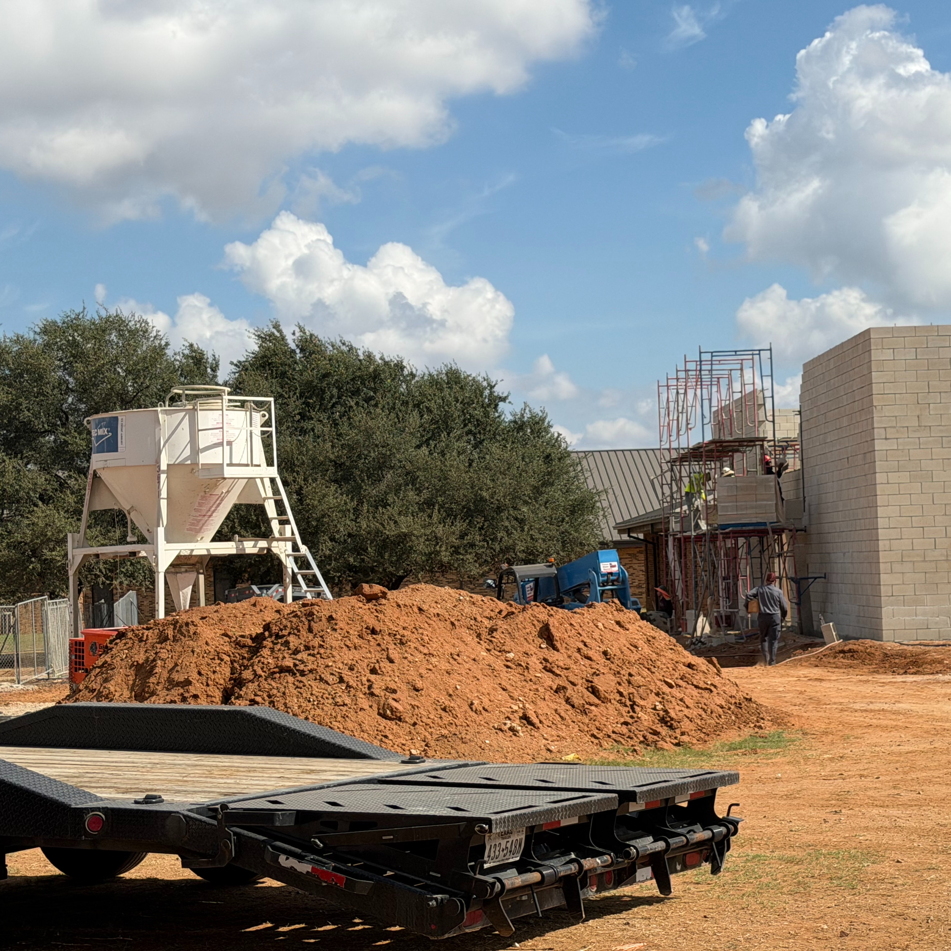 A construction site with a building under construction and a large pile of dirt in front.