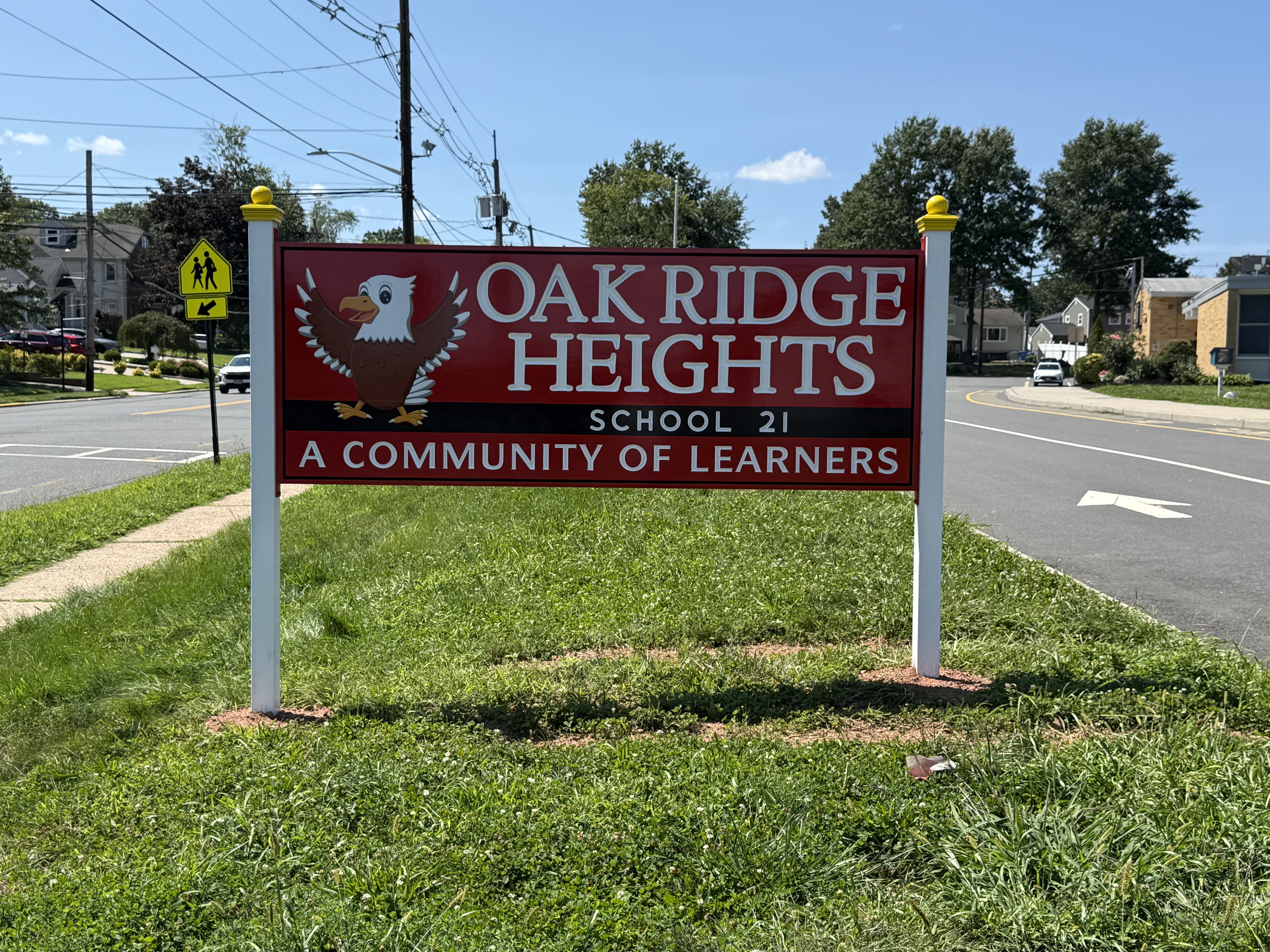 Signboard for Oak Ridge Heights School 21, featuring an eagle logo, on a green lawn beside a street.