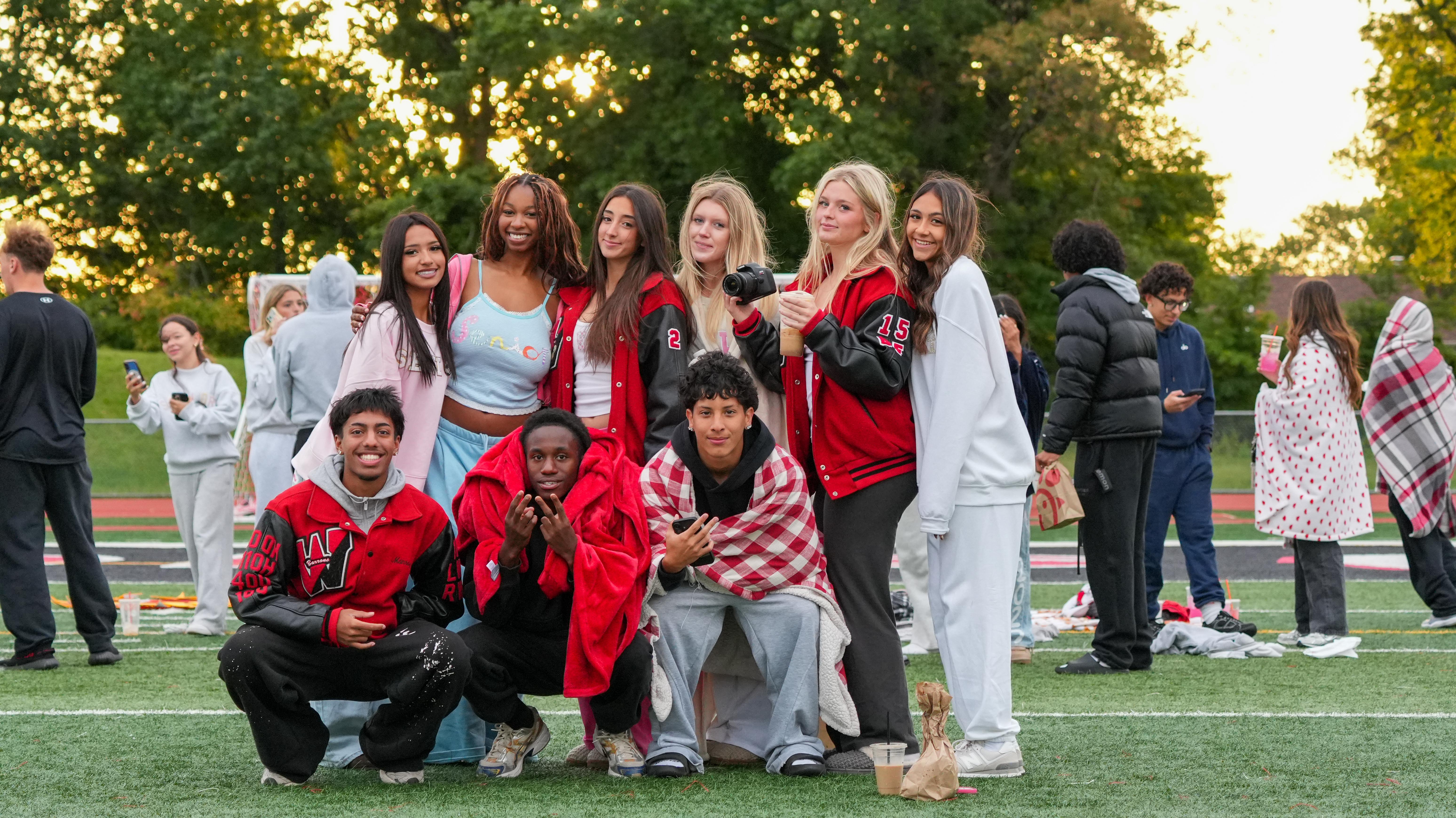 Group of people in matching outfits, some kneeling and some standing, on a football field with trees.