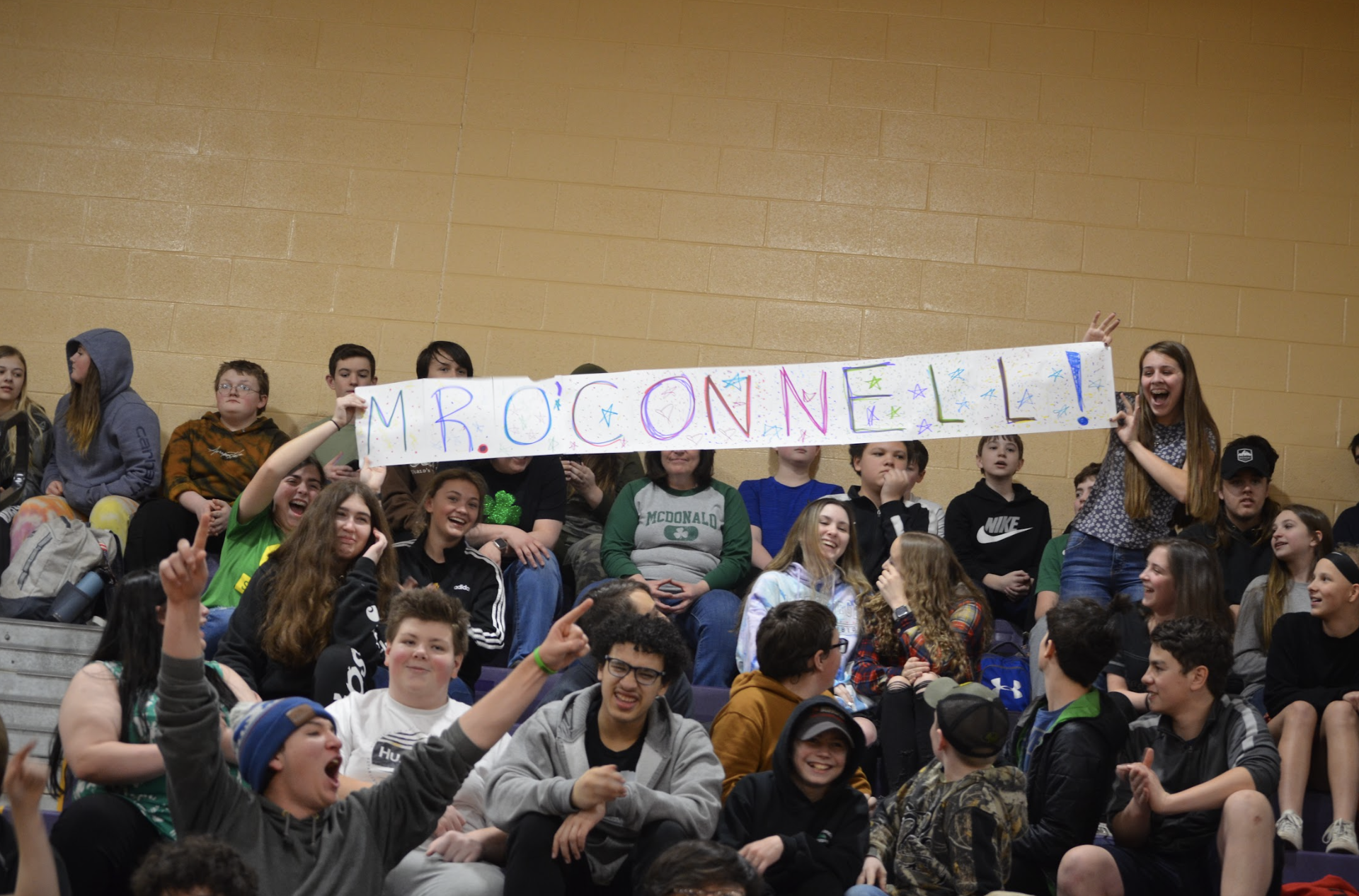 students holding a sign for a teacher at the pep rally
