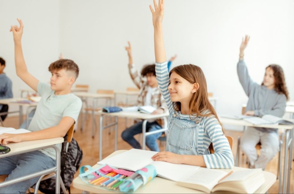 students in a classroom, smiling with hands raised