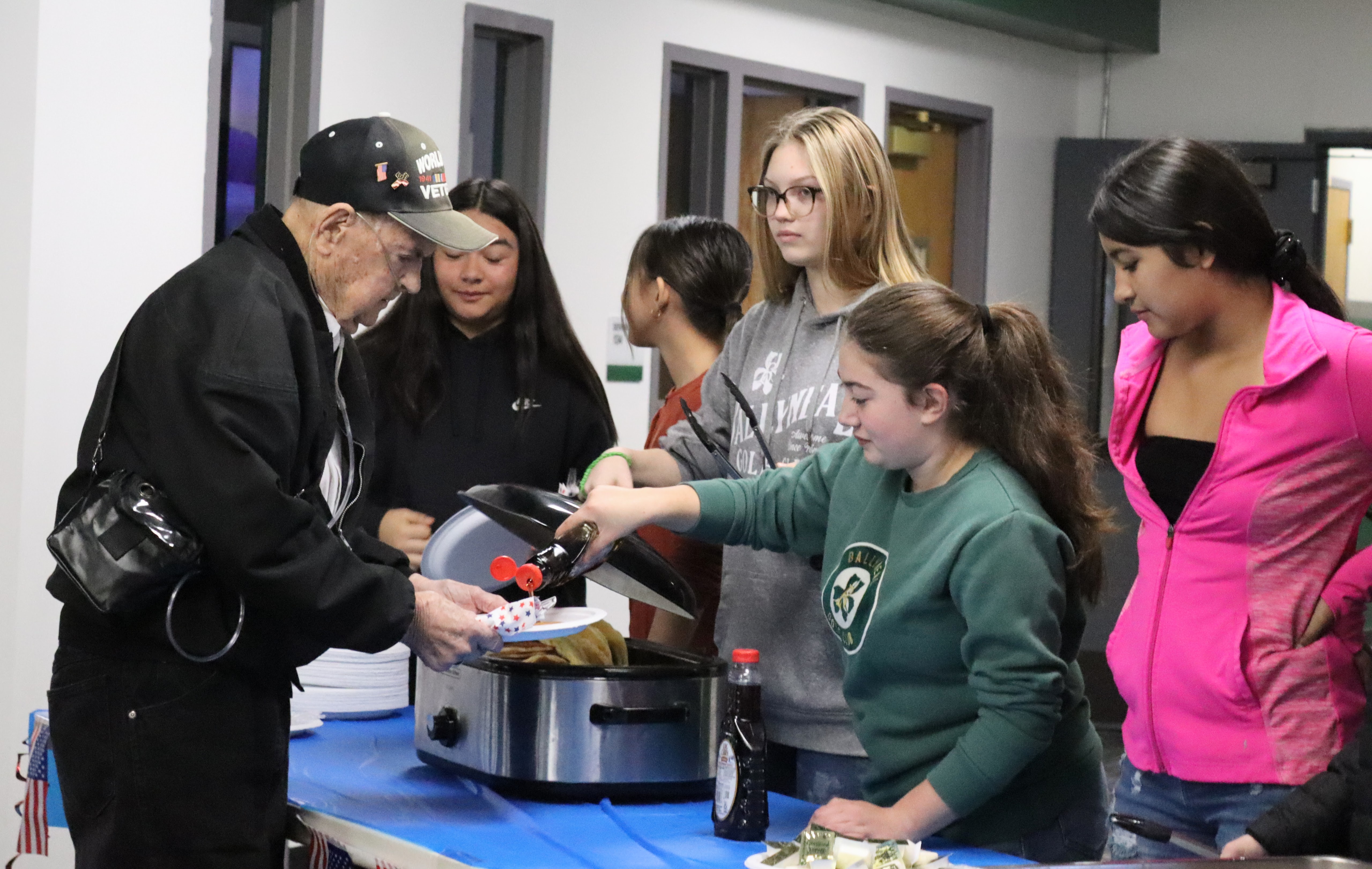 Students serving pancakes to a veteran