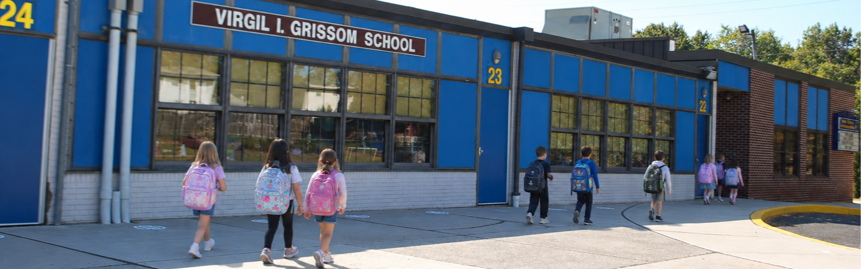 Children wearing backpacks walking into a school with "VIRGIL I. GRISSOM SCHOOL" on the front.