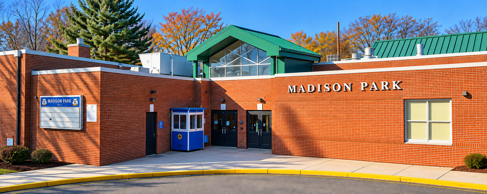 Brick building with green roof and glass doors. "MADISON PARK" above the entrance. Blue and white booth. Trees behind.