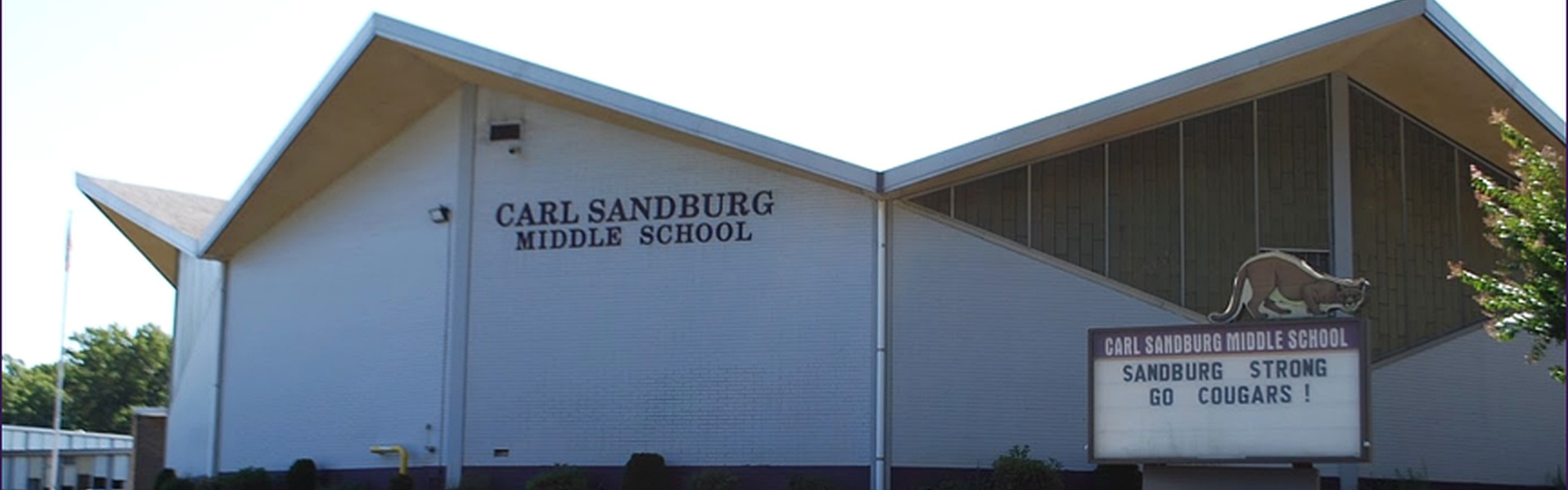 A school building with a triangular roof. Text reads "Carl Sandburg Middle School" on the wall. Sign in front.