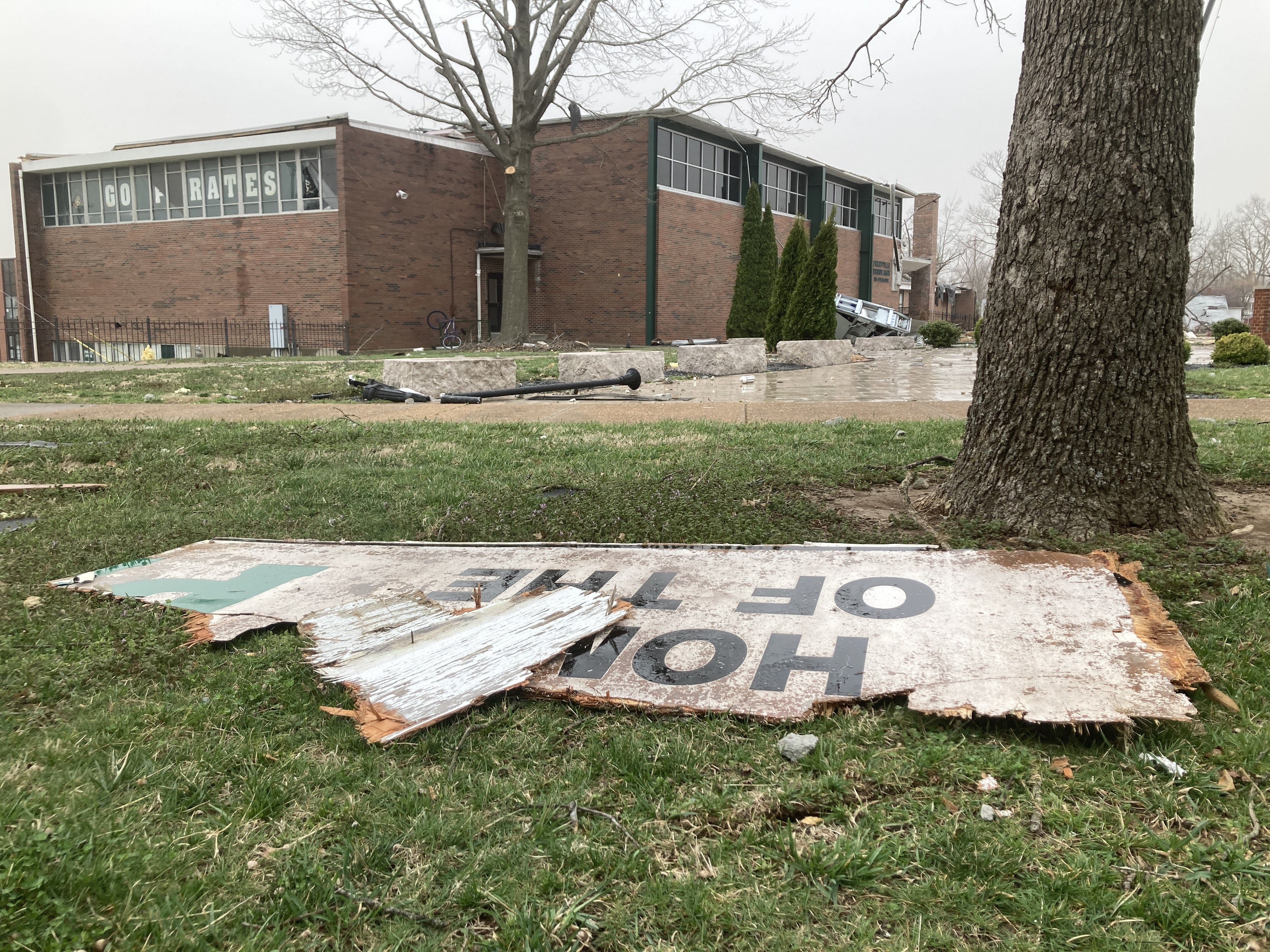 A tattered "Home of the Pirates" sign lies in the foreground with a tornado-ravaged  PHS in the background.