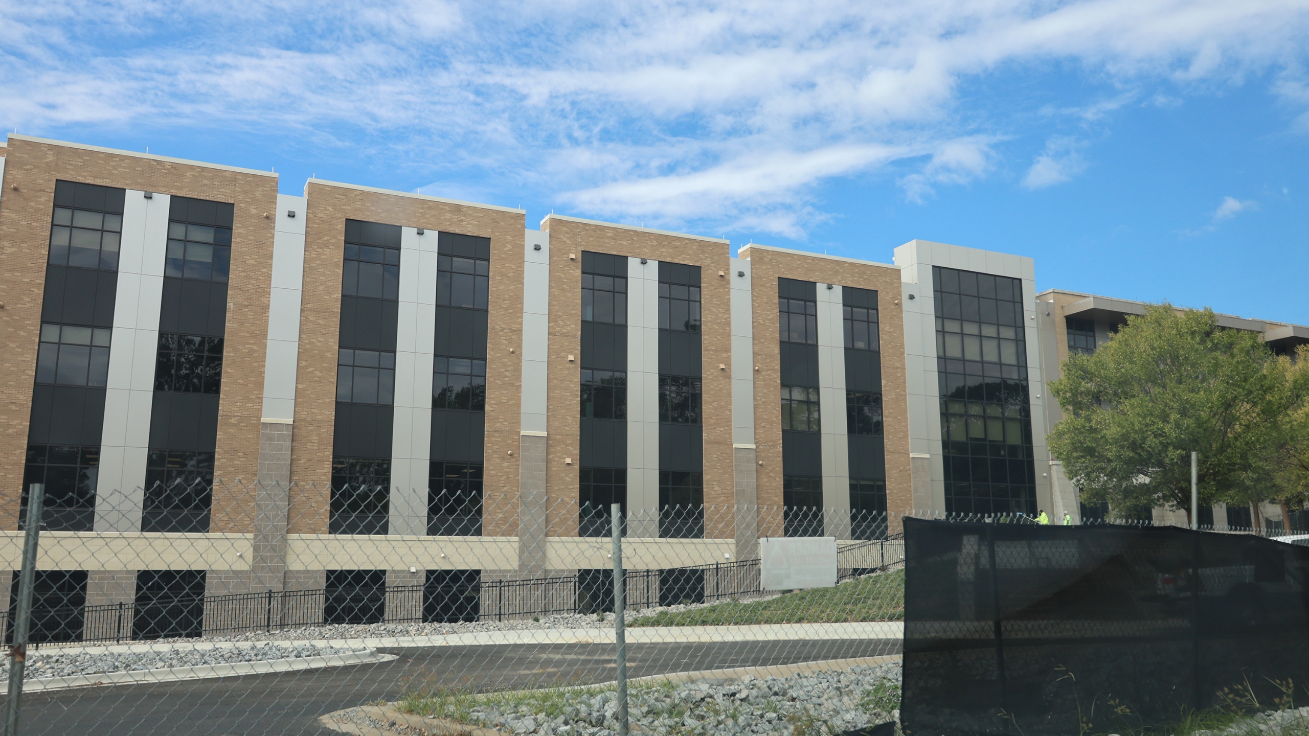 A large, multi-story building with many glass windows, fenced off with a chain-link fence.