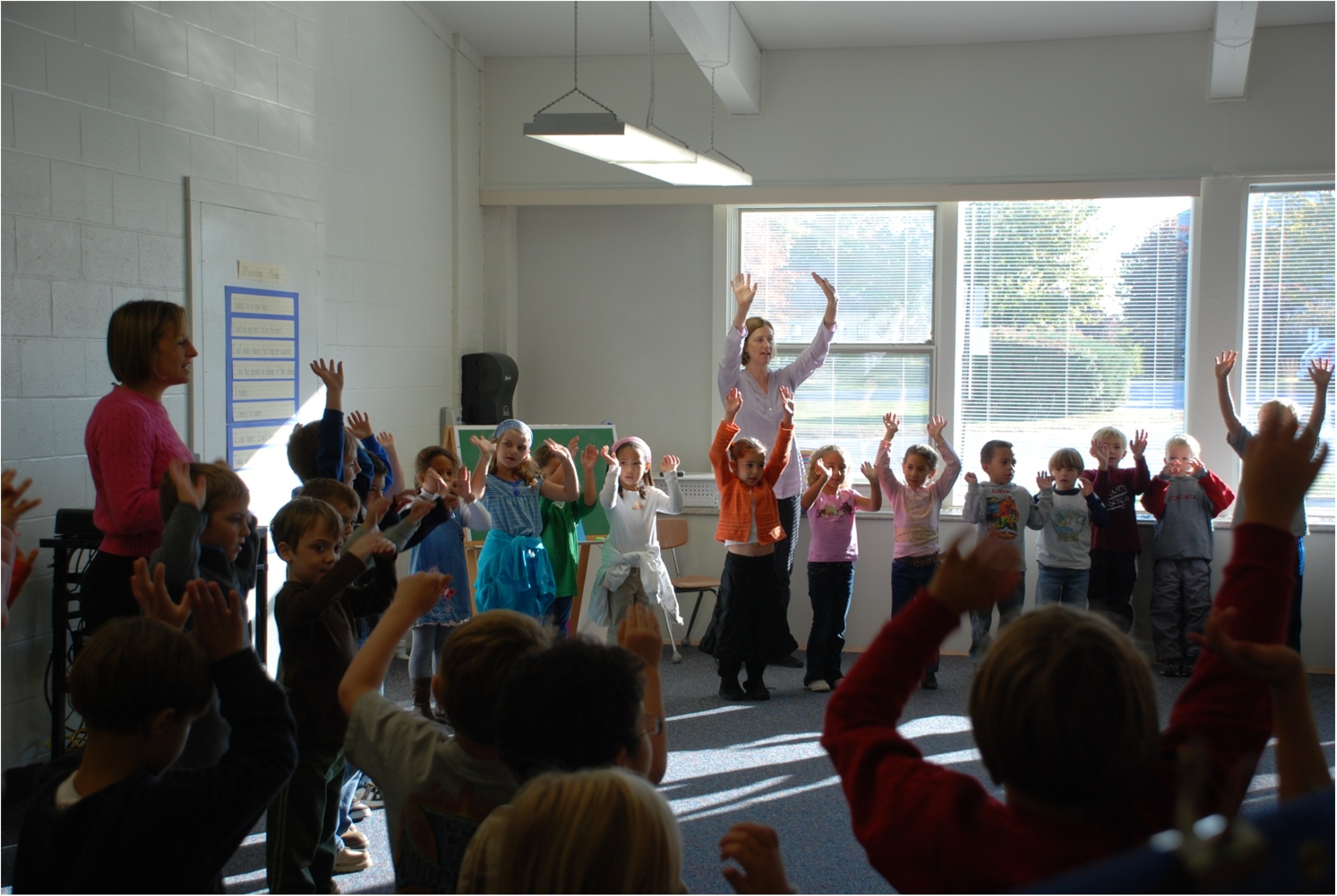 A photo of a class with kids standing up making an exercise.