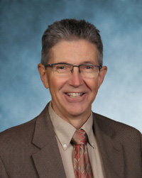 headshot of man smiling, tie, glasses