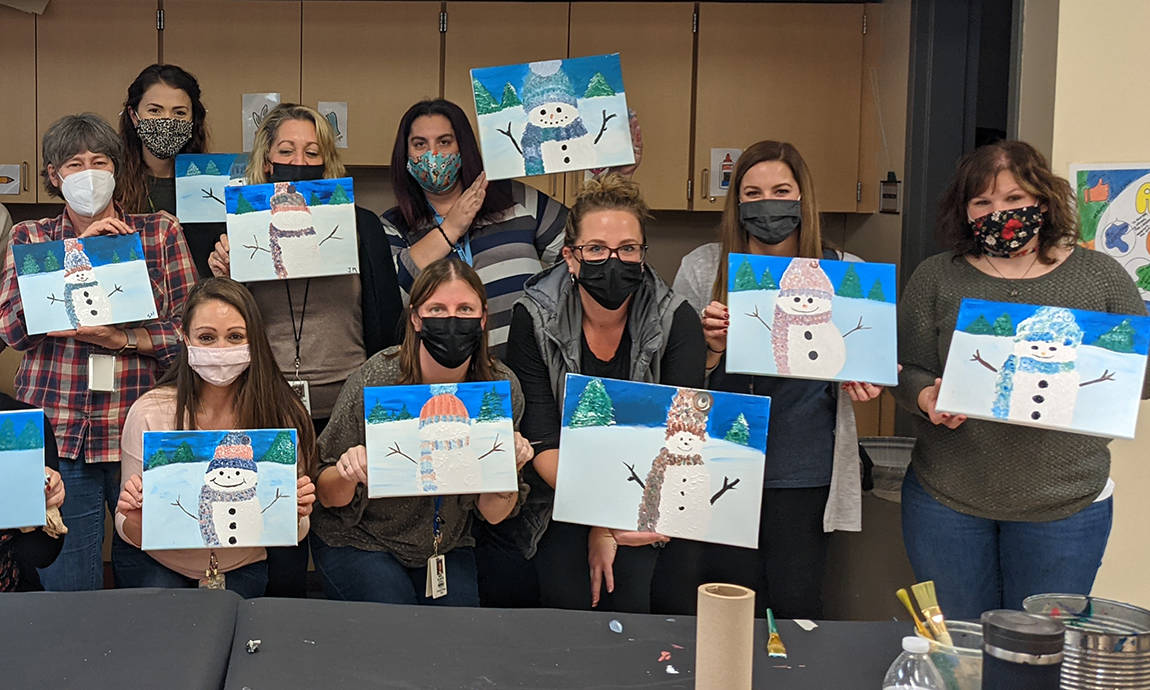 group of masked people holding up painting of snowmen