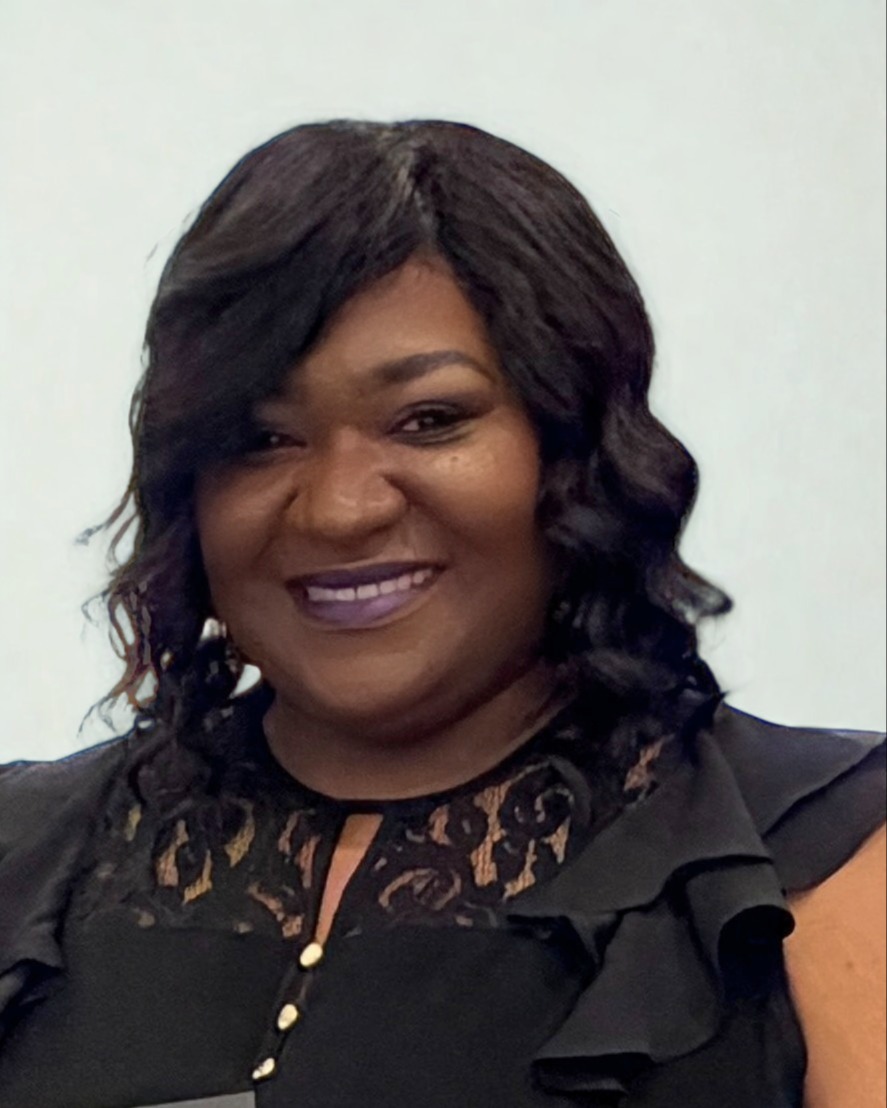 Woman with short, curly black hair, wearing a black blouse with ruffled edges, smiling for the camera.