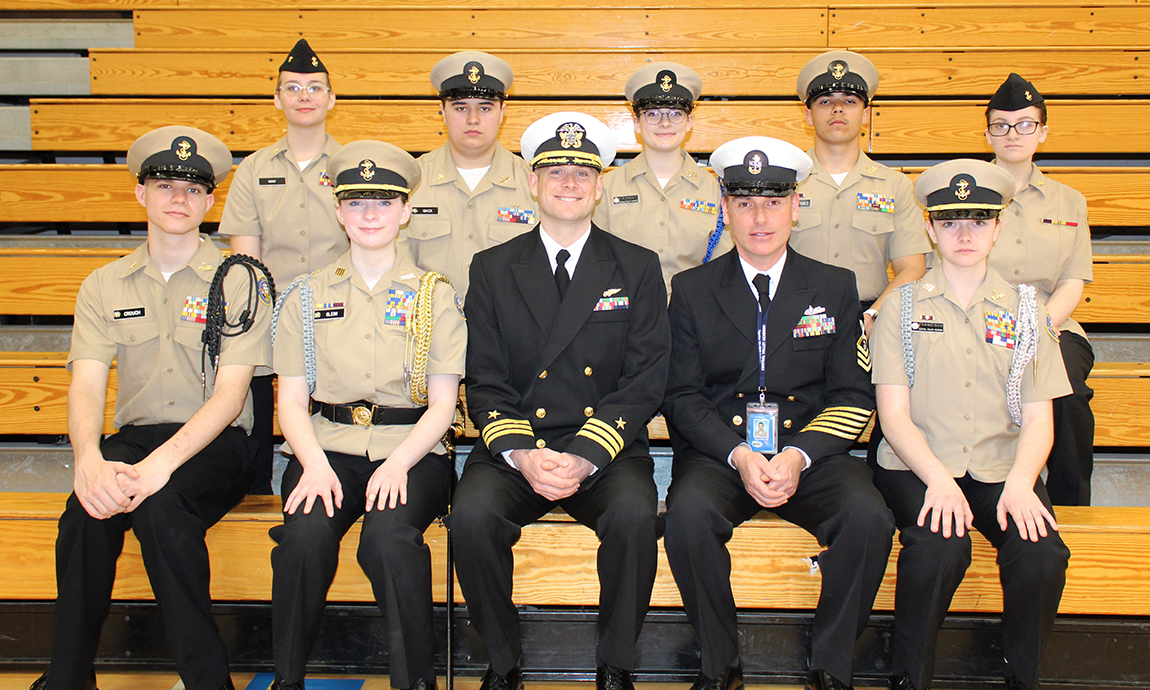 8 cadets, 1 chief, 1 commander seated on gym bleachers