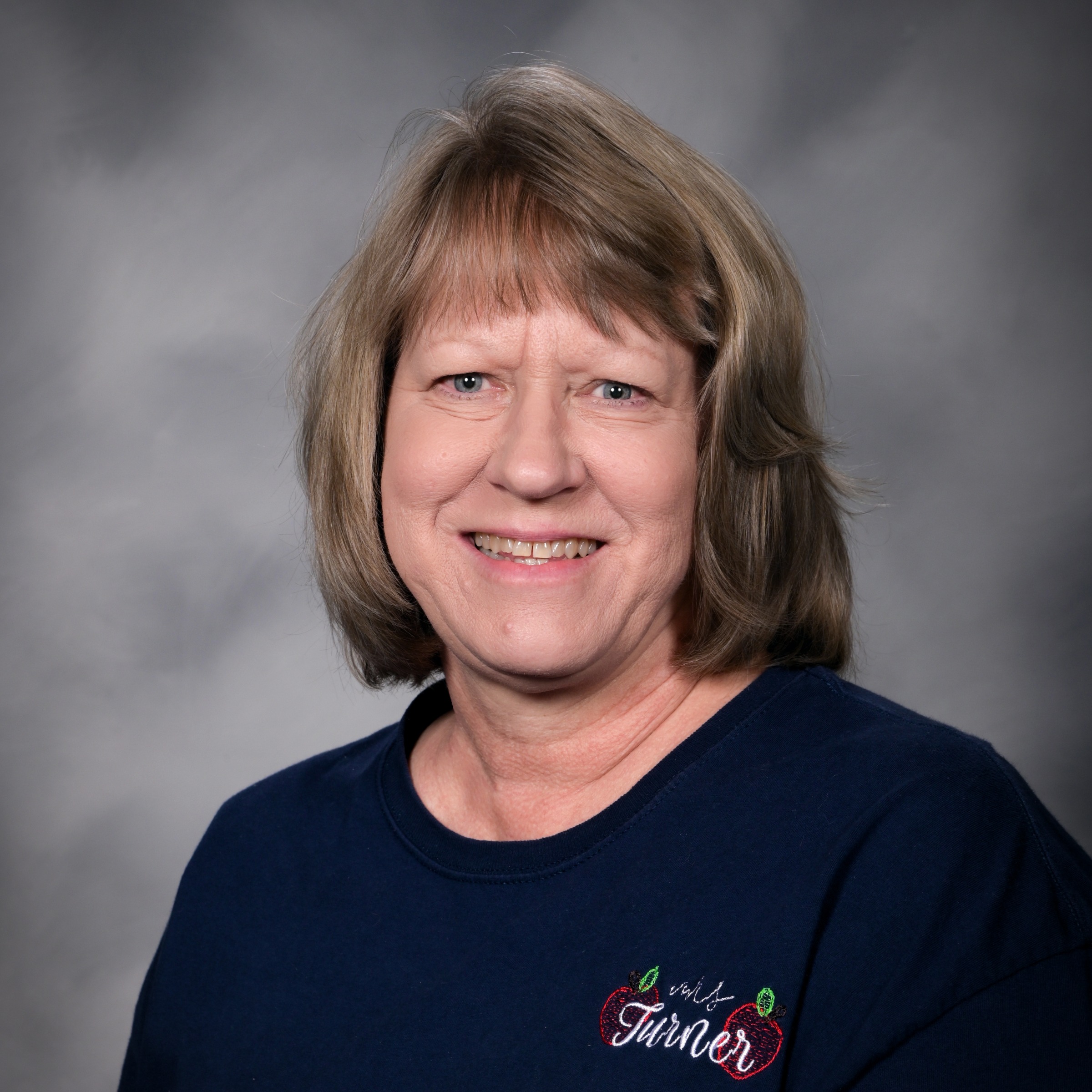 A woman with short blonde hair smiling at the camera. She wears a navy blue shirt with a red logo.