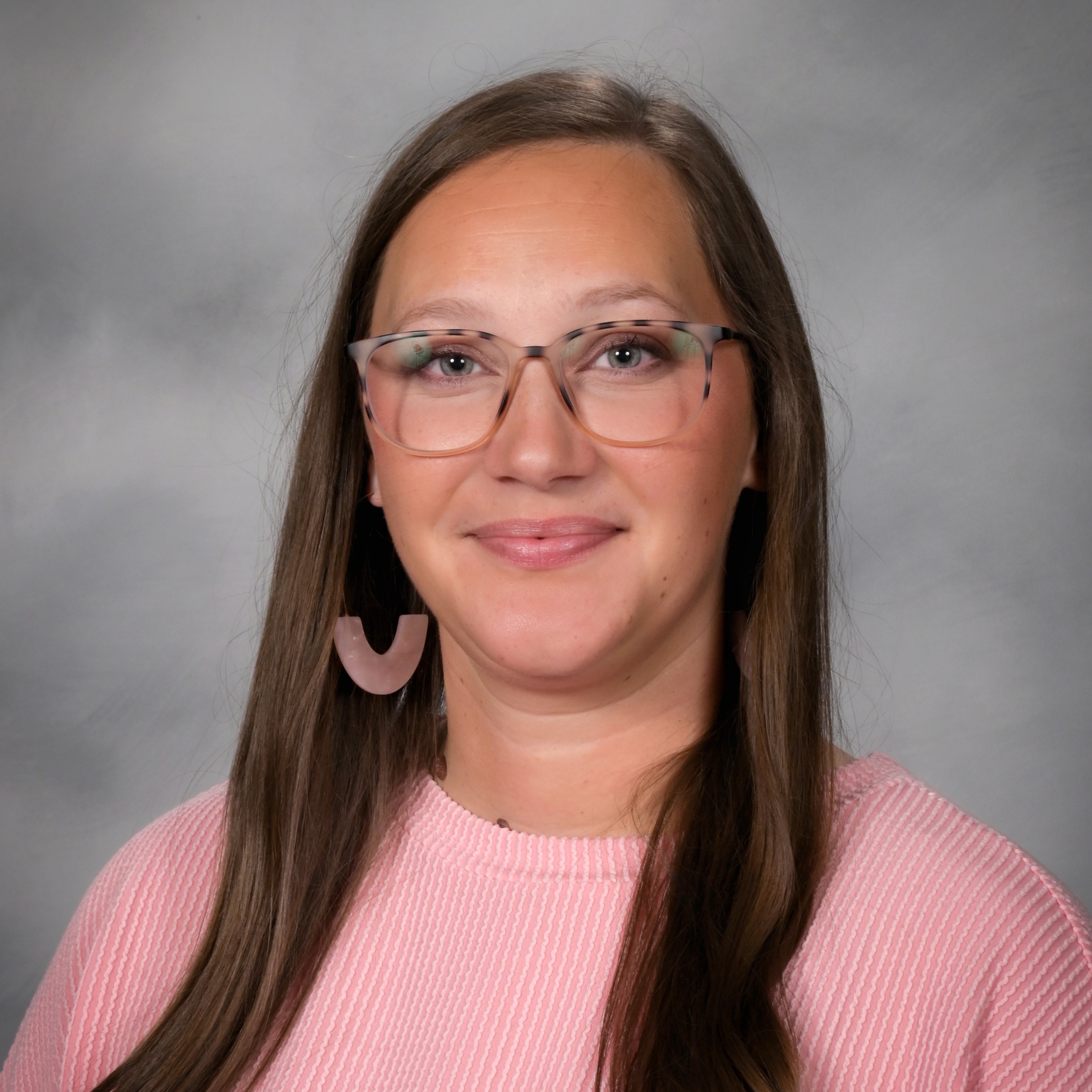 Woman with long dark hair and glasses wearing a pink sweater and pink earrings.