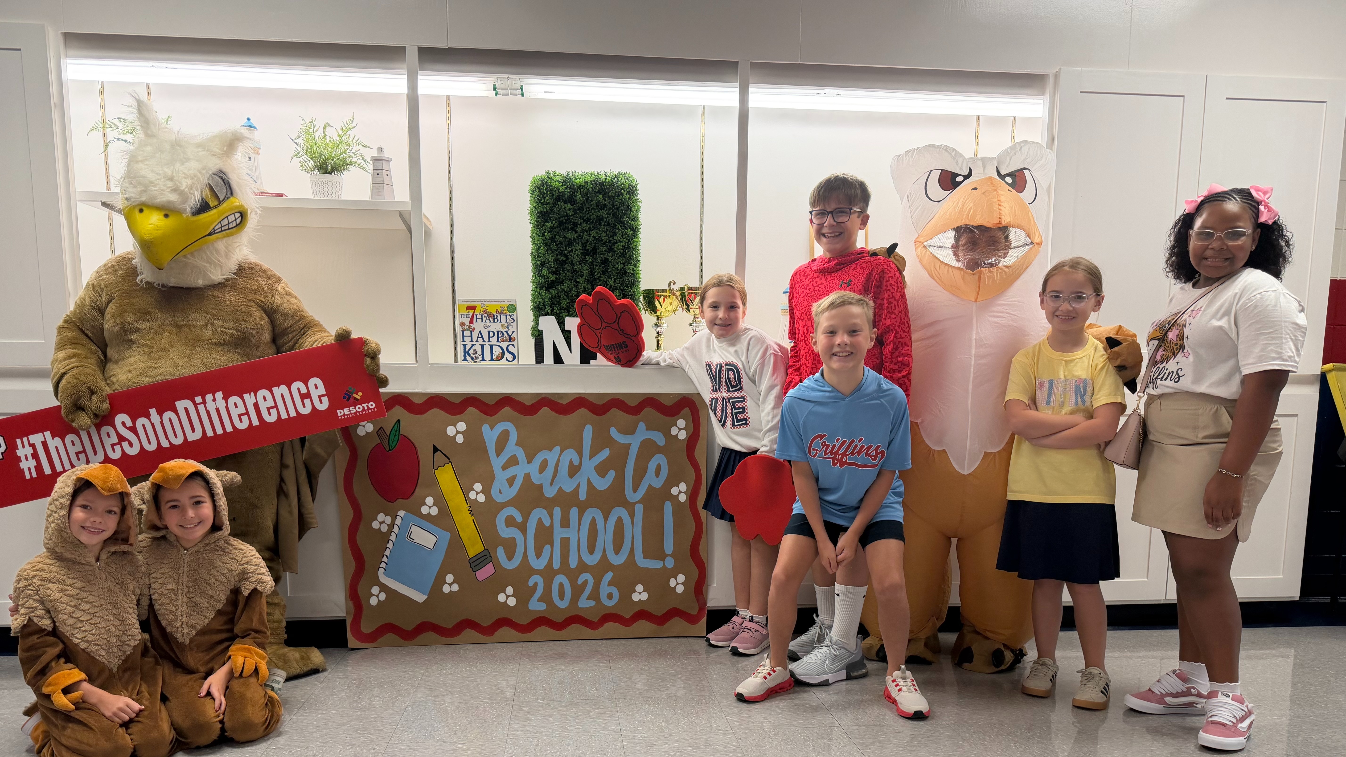 A group of children and mascots in a room with a sign reading "Back To School 2026" and "Those So Different"