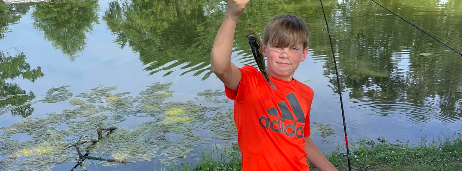 student shows fish he caught with pond in background