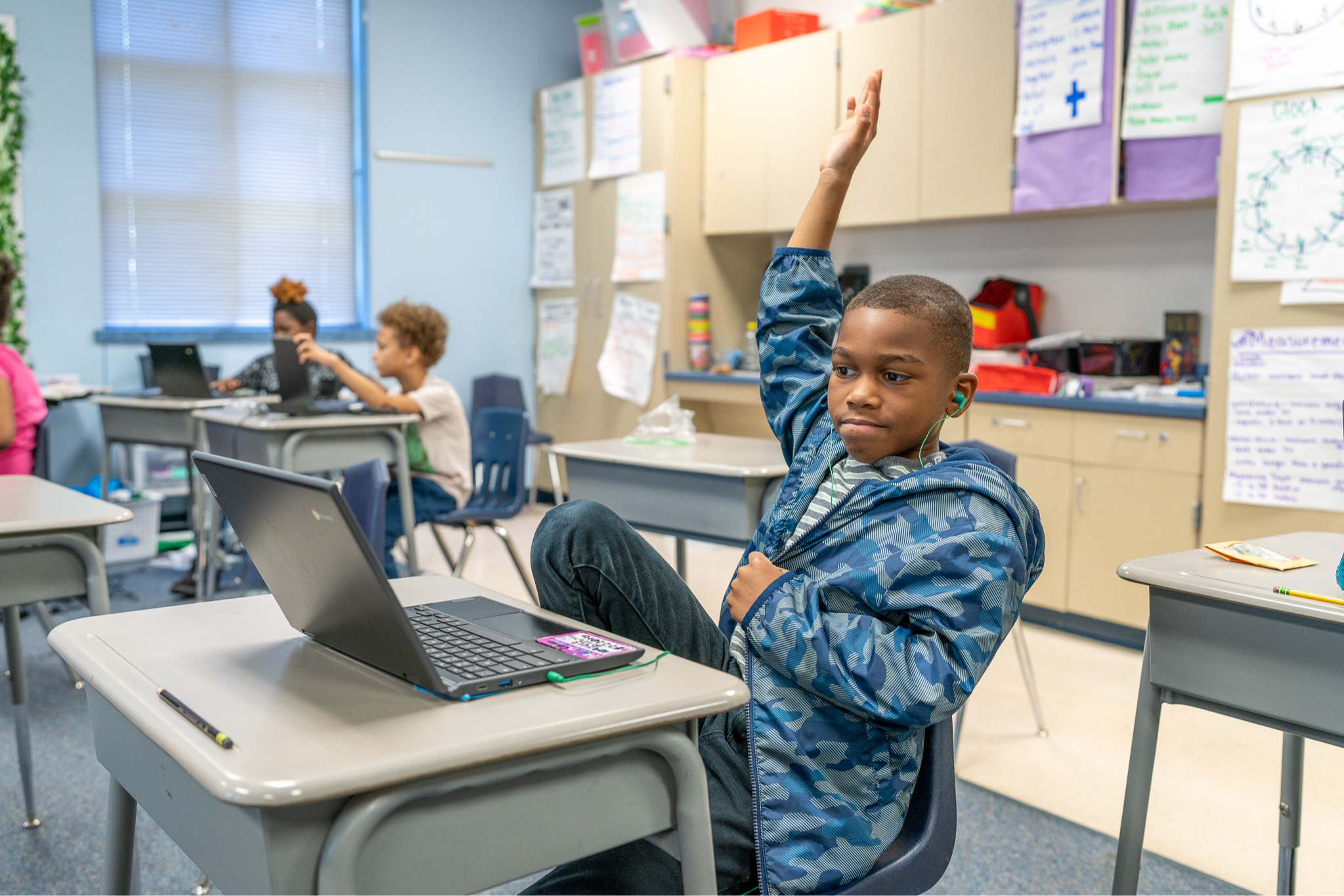 African American elementary age boy sitting at a desk with his hand raised