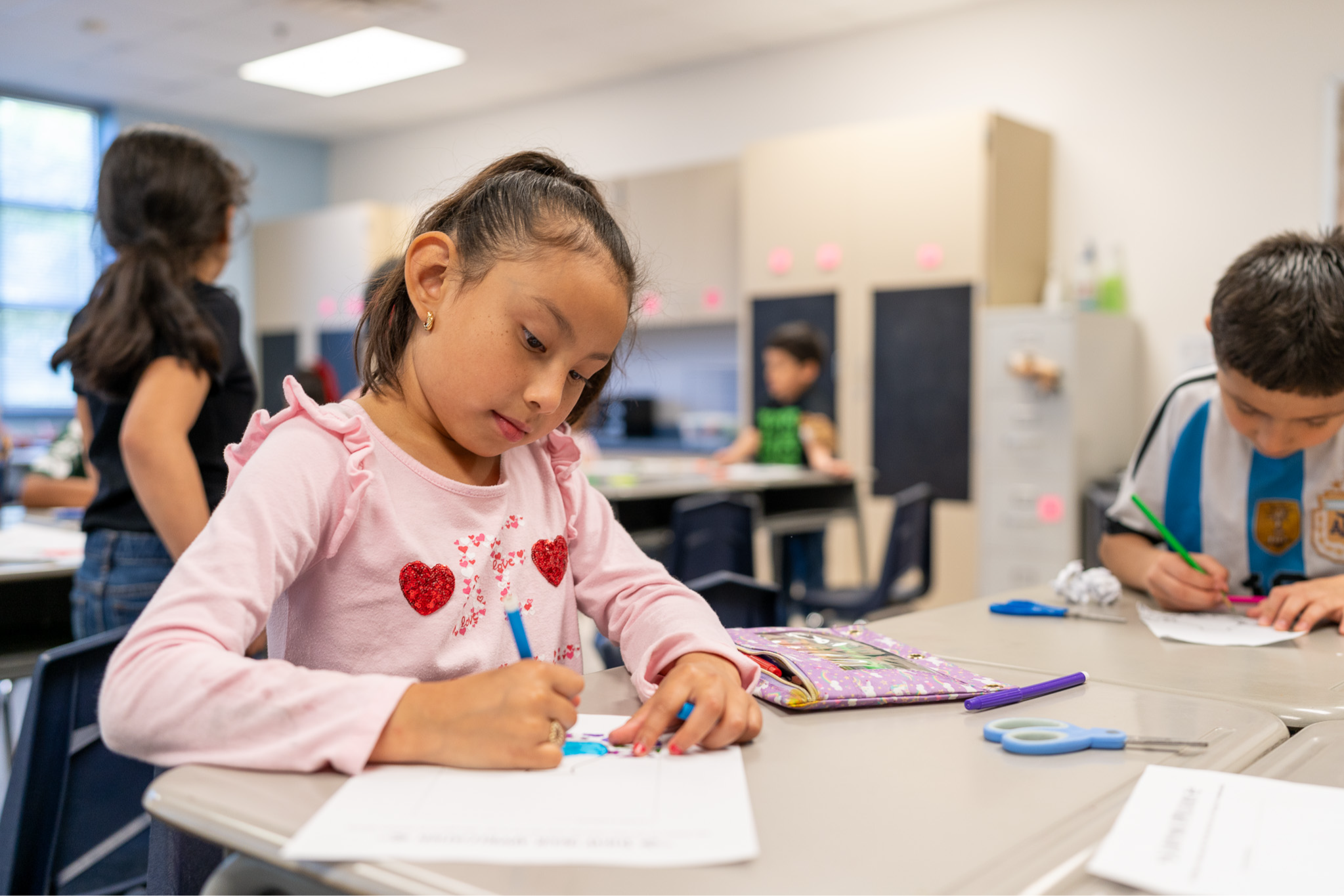 elementary age girl sitting at a desk coloring a paper