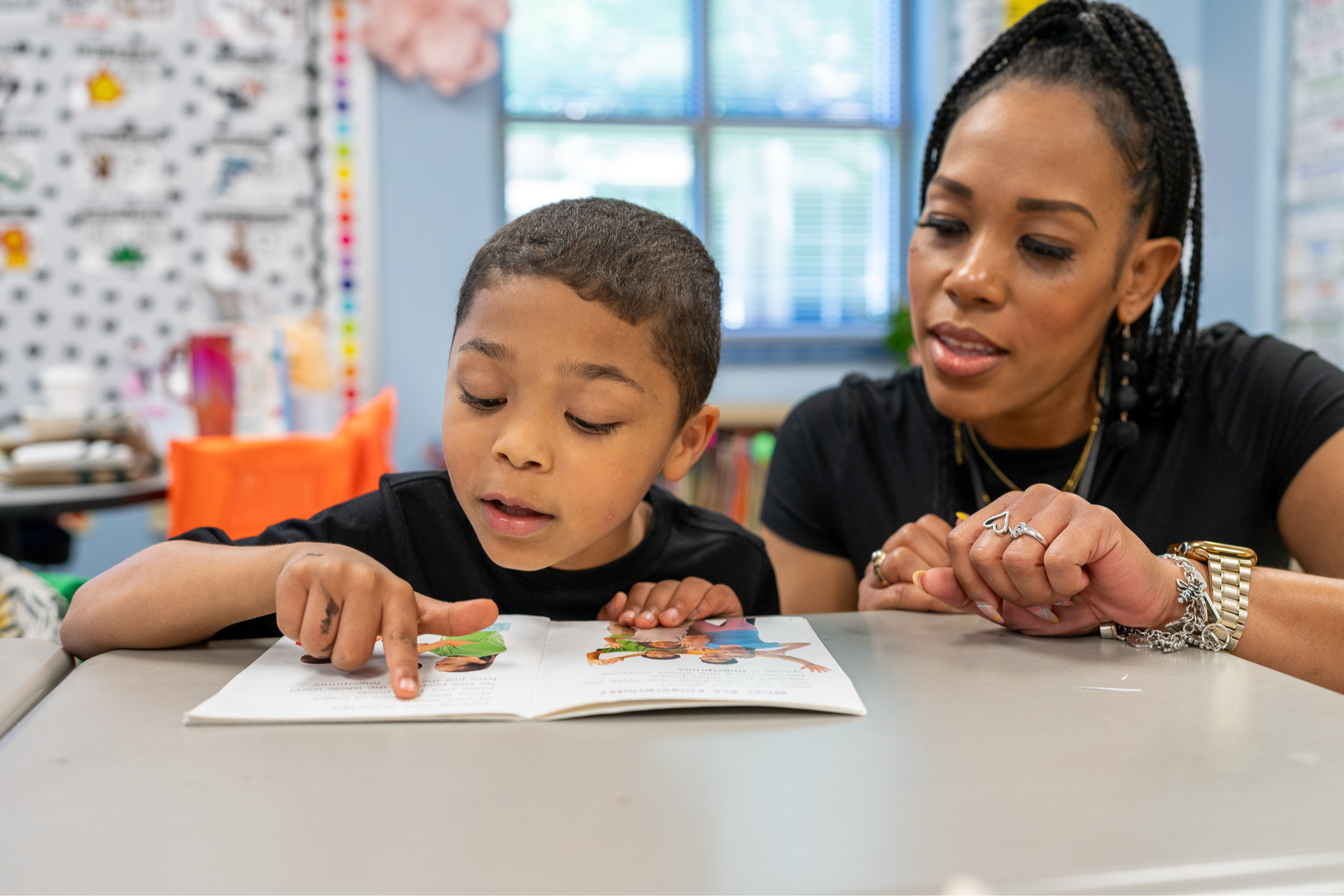 elementary age boy sitting at desk reading with a woman kneeling next to him