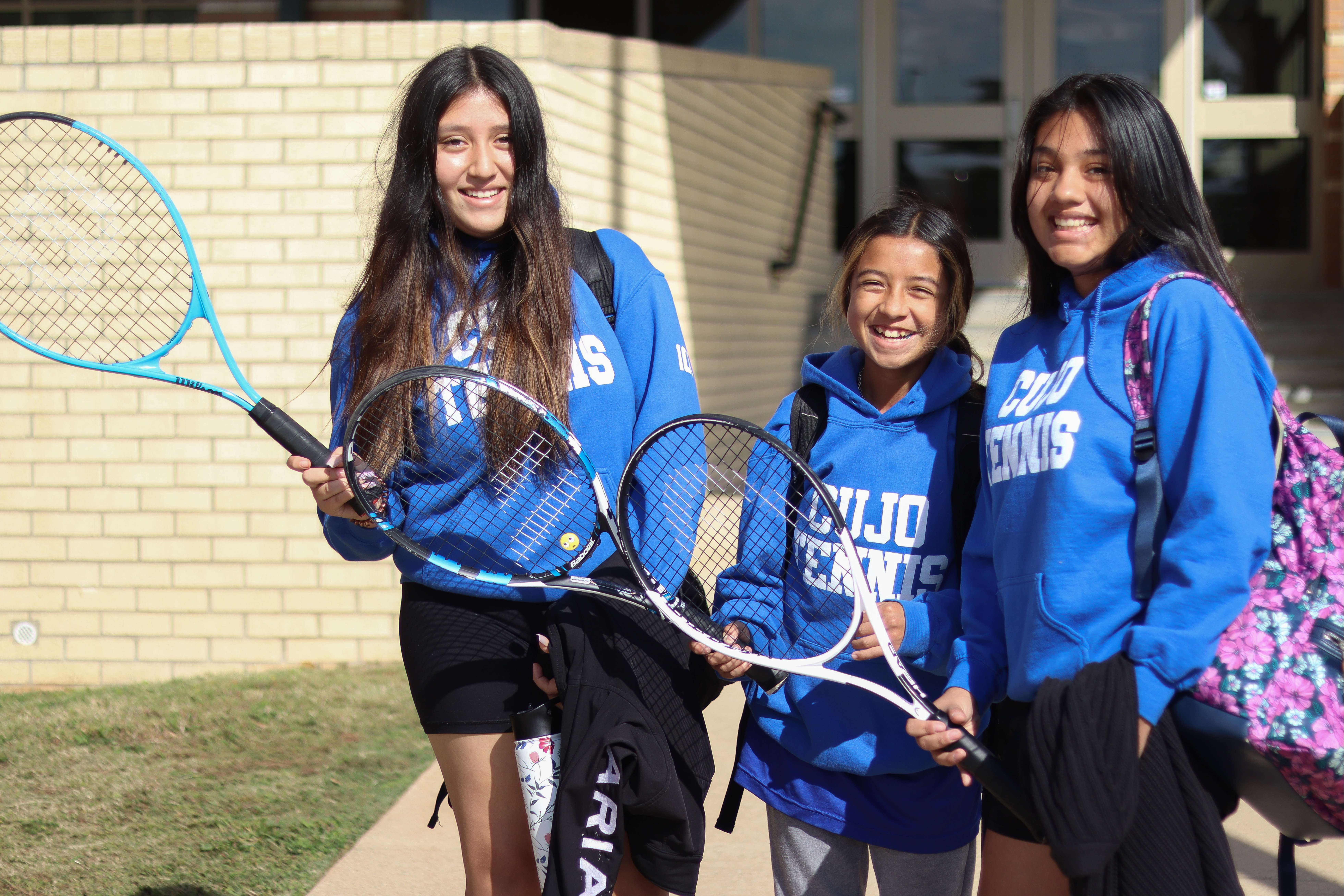 three teenage girls holding tennis racquets and smiling