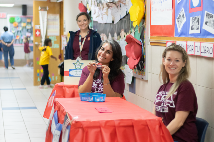 birdwell staff at voting simulation booth holding stickers that say "vote". for more information, contact the front office. 