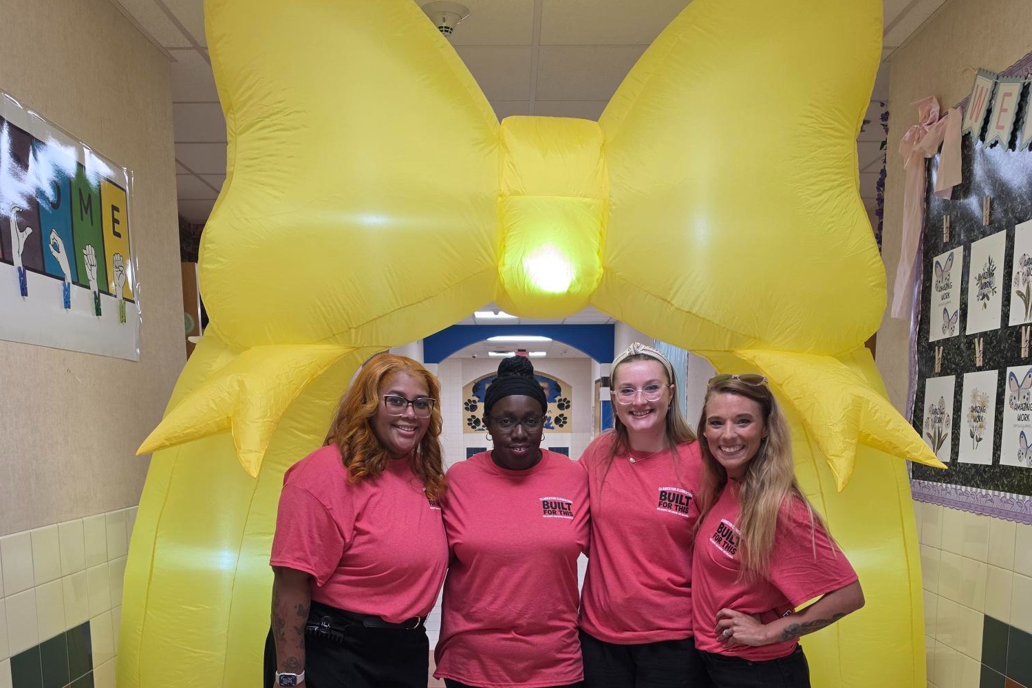 Teachers gather before a big yellow bow at back to school event.
