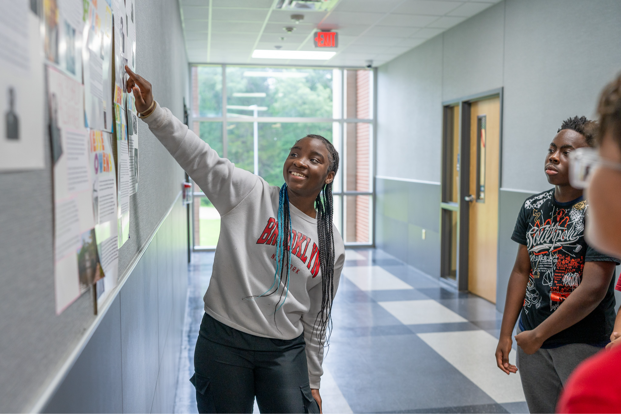 teen girl points at poster in school hallway as other teens look on